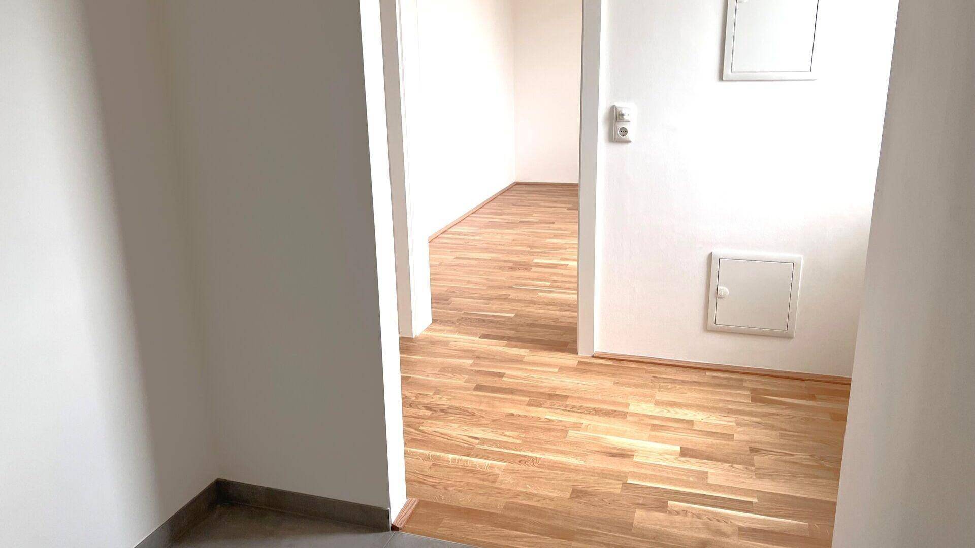 Gangbereich mit Holzboden und weißen Wänden, der den Übergang zu weiteren Zimmern bildet.