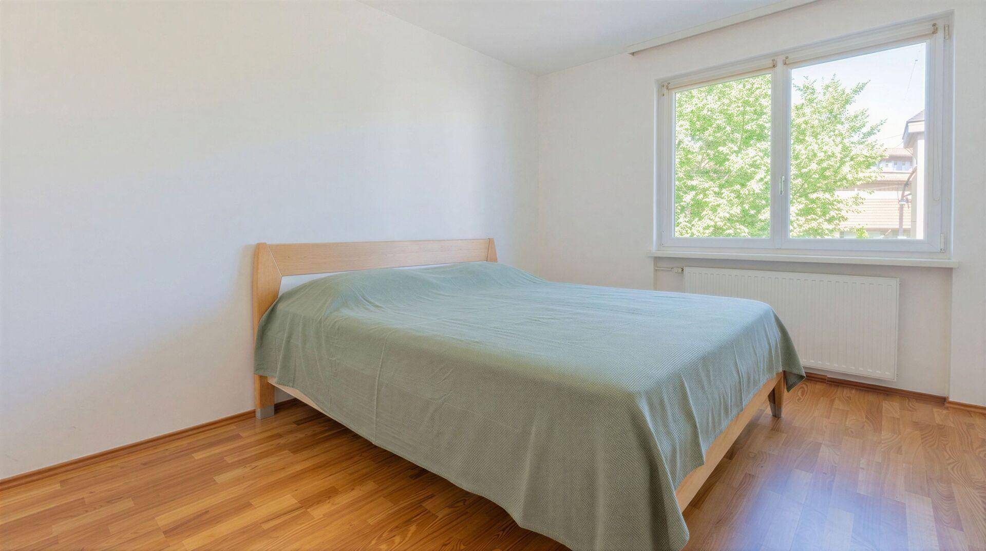 Schlafzimmer mit Holzbett, Parkettboden und großem Fenster mit Blick ins Grüne.