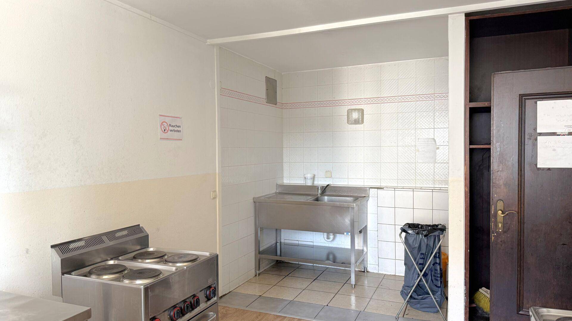 Einfache Küche mit Edelstahlspüle, Kochplatten und gefliesten Wänden.