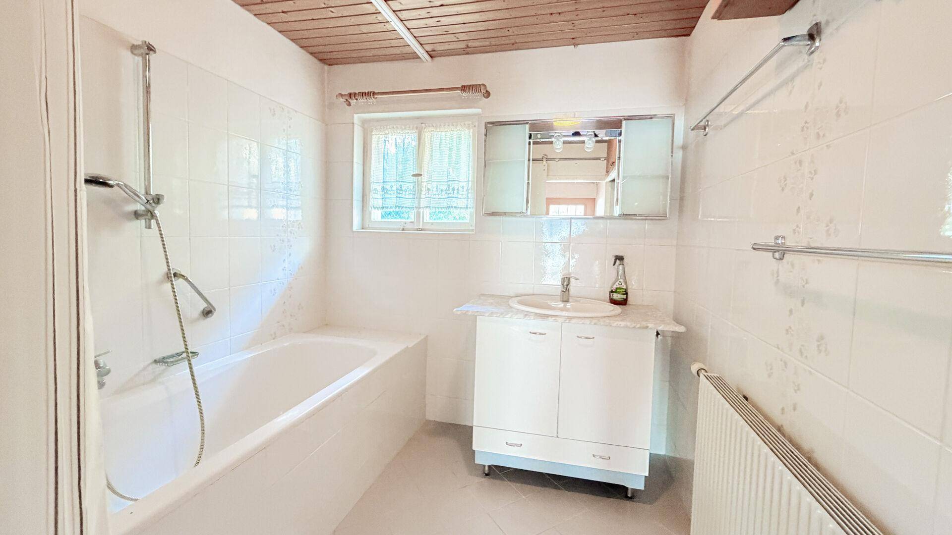 Badezimmer mit Badewanne, Dusche, Waschbecken und Spiegelschrank unter Holzdecke.
