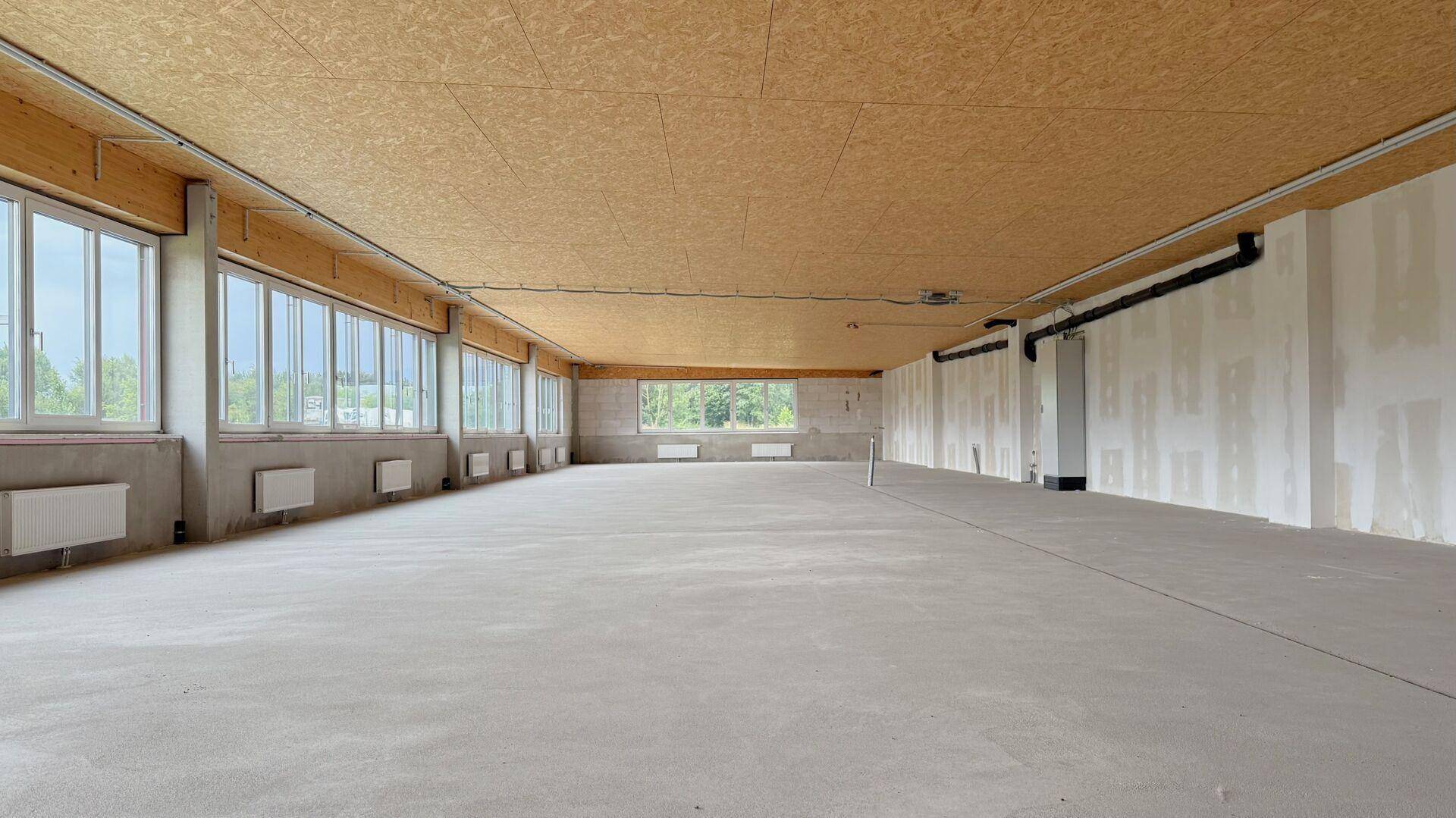 Weitläufiger, unmöblierter Gewerberaum mit Sichtbetonboden und Holzdecken, bereit für den Innenausbau.