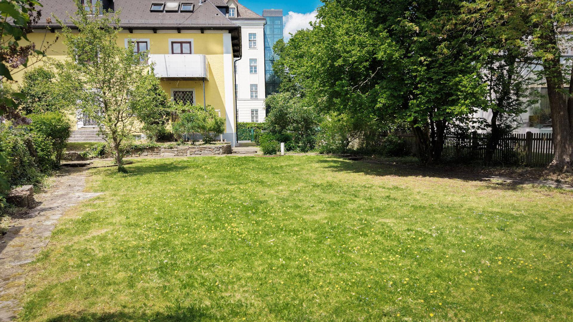 Großer grüner Garten mit Rasenfläche und Bäumen hinter dem Haus.