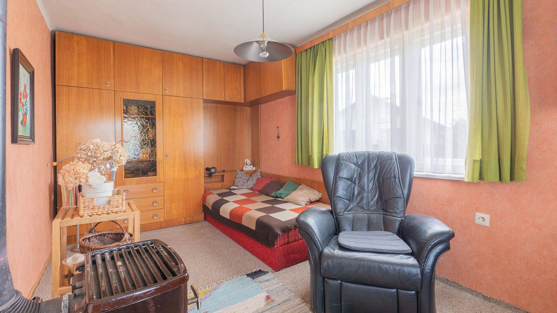 Schlafzimmer mit Einbauschränken, Bett und Sessel, in warmen Farbtönen gehalten.