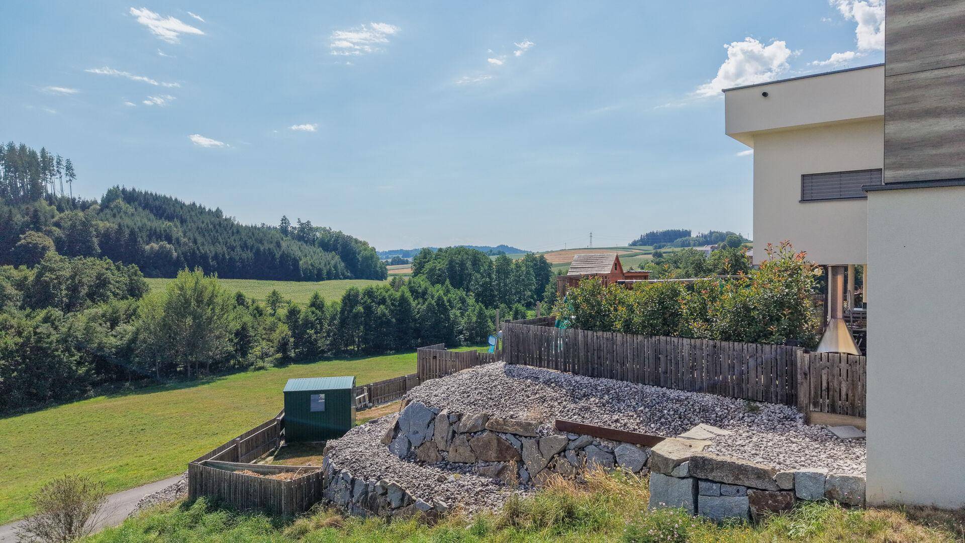 Seitenansicht des Hauses mit weitem Blick über grüne Felder und Wälder in der ländlichen Umgebung.