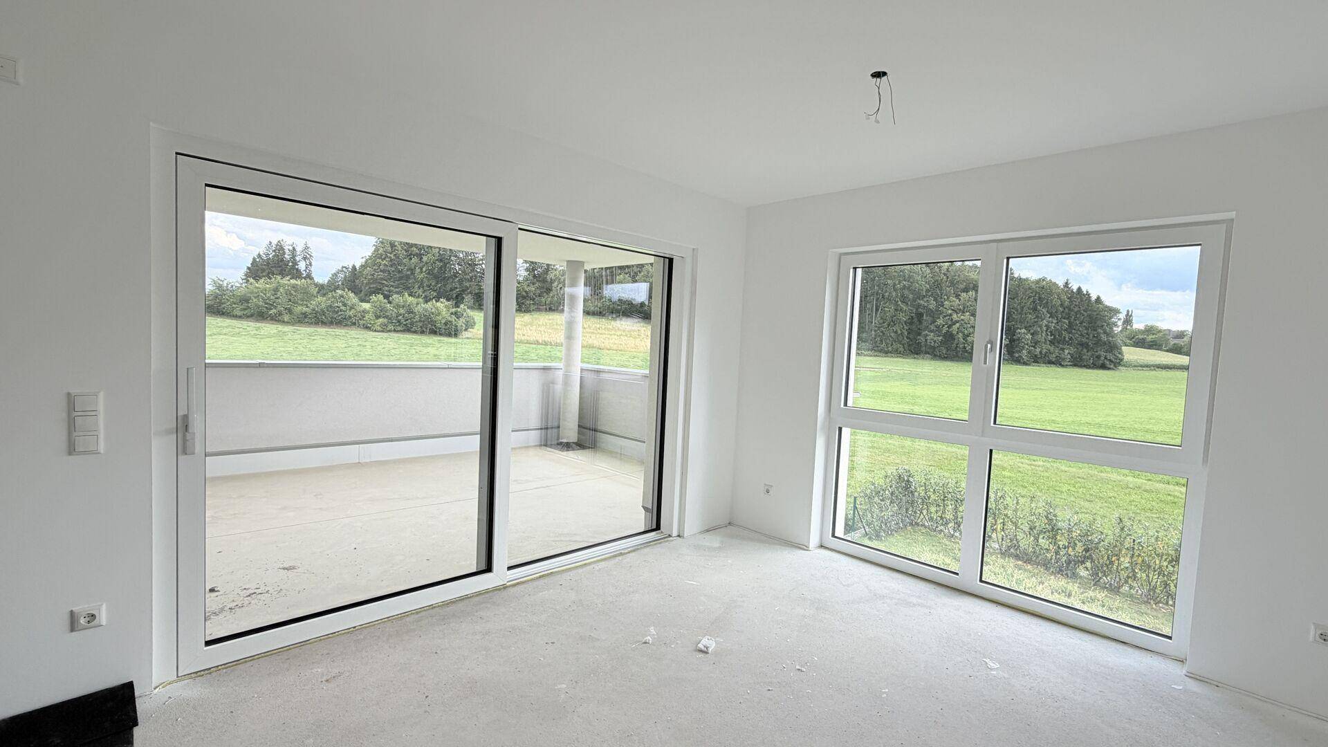 Heller, unmöblierter Raum mit großen Schiebetüren zum Balkon und weitem Blick ins Grüne.