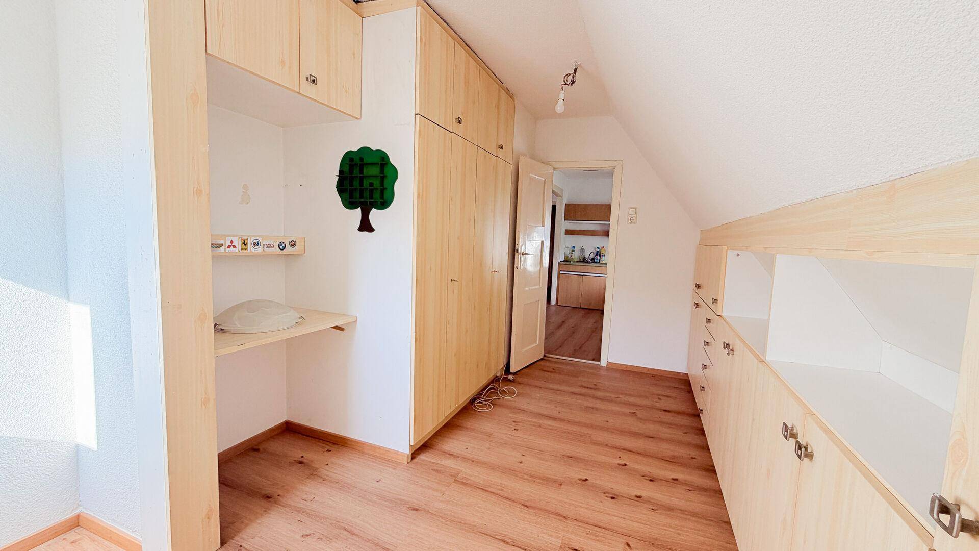 Zimmer mit maßgefertigten Holzschränken, integriertem Schreibtisch und schräger Dachschräge.
