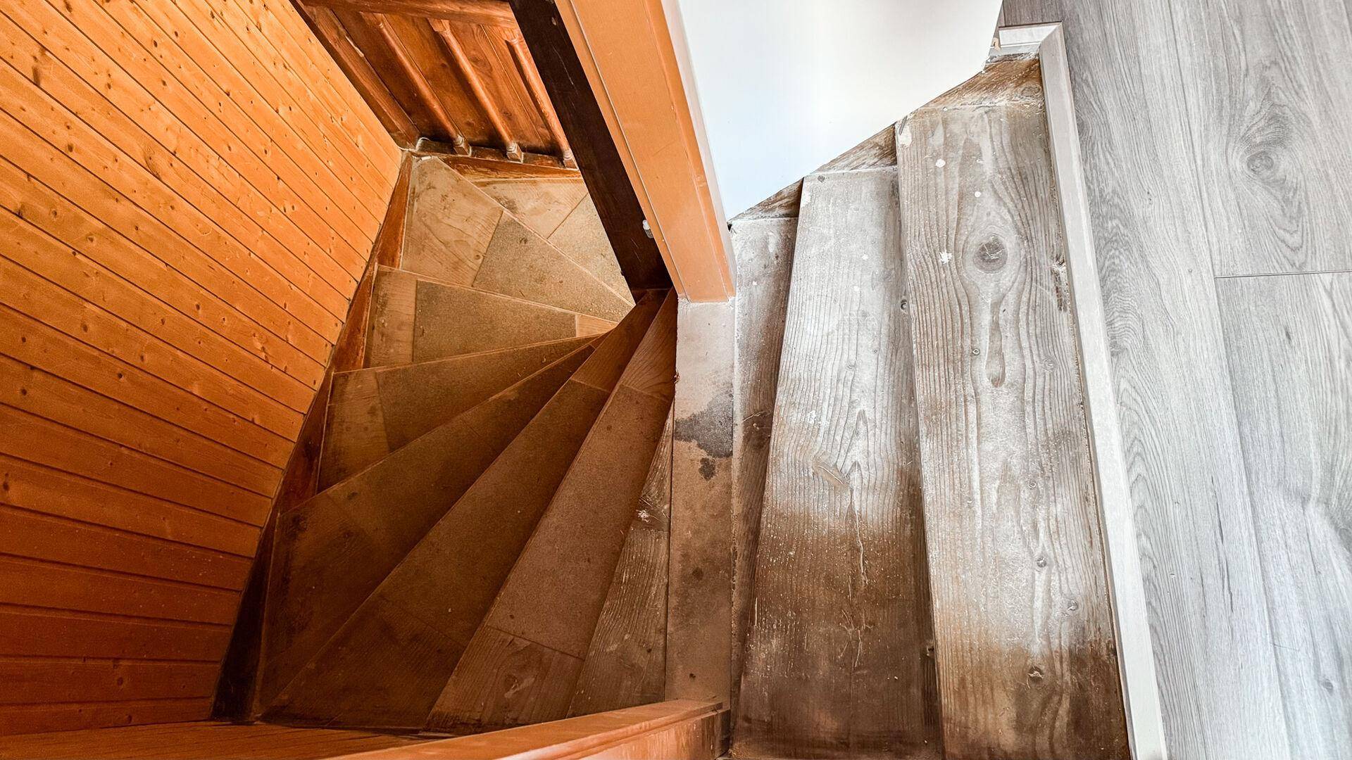 Holztreppe mit abgenutzten Stufen und Holzverkleidung an den Wänden.