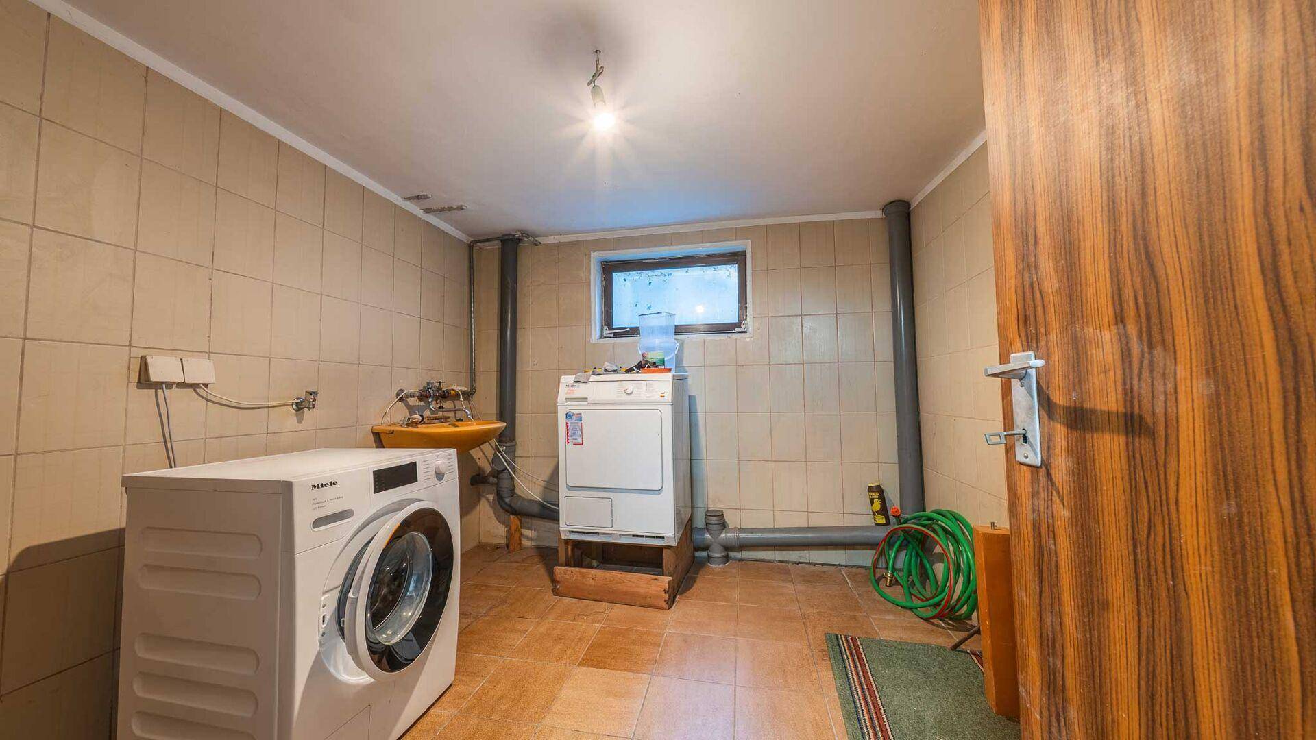 Funktionale Waschküche mit Waschmaschine, Trockner und Spülbecken, ausgestattet mit Fliesen.
