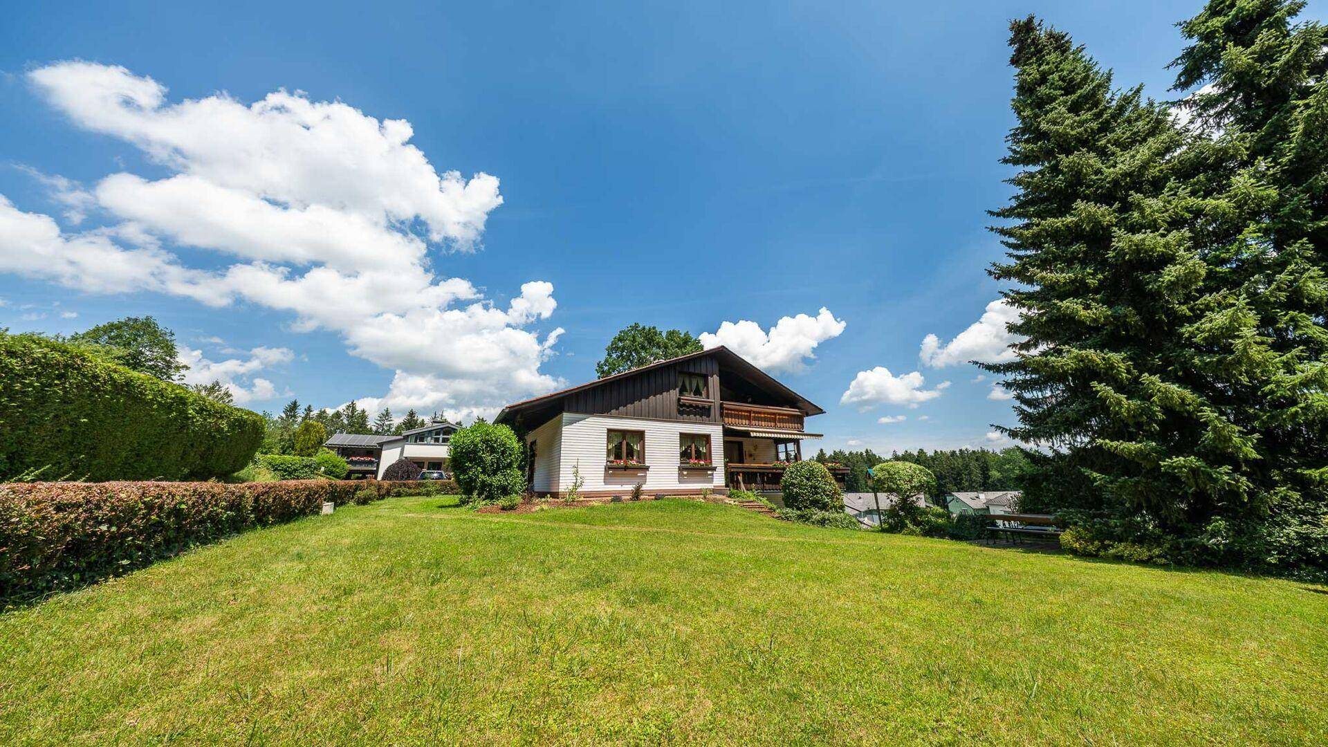 Freistehendes Haus mit großem Rasen und hohen Bäumen, umgeben von einer weitläufigen grünen Landschaft.