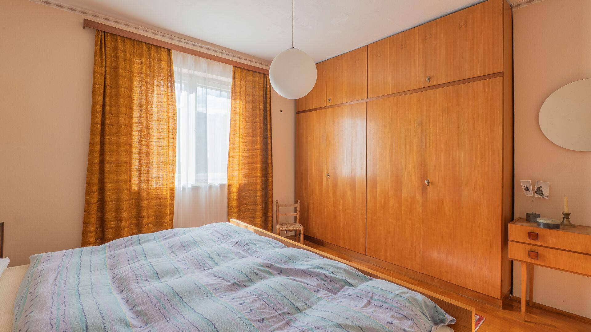 Schlafzimmer mit großem Bett, Einbauschränken und gelben Vorhängen.