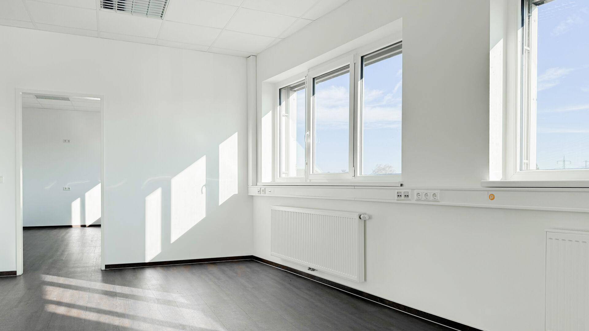 Heller Büroraum mit großen Fenstern und dunklem Boden, ideal für eine produktive Arbeitsumgebung.