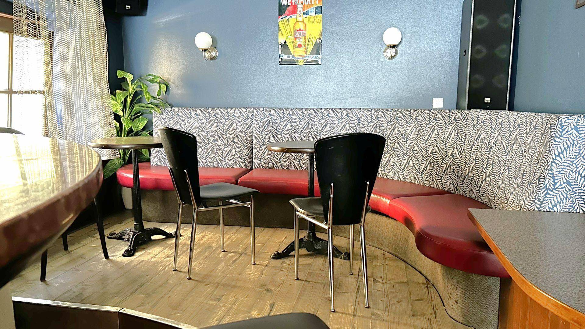 Gemütlicher Sitzbereich in der Bar mit einer geschwungenen Bank, kleinen Tischen und blauen Wänden.