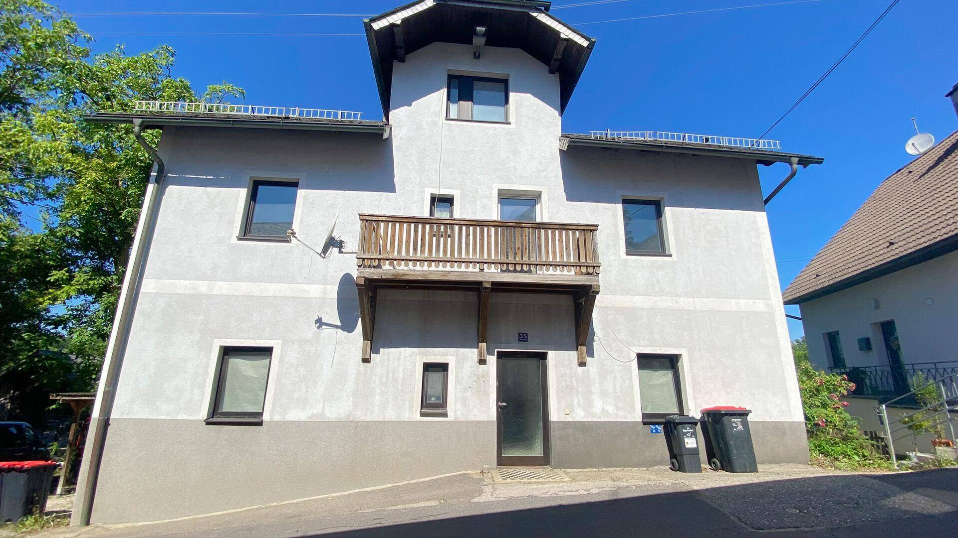 Mehrstöckiges Gebäude mit heller Fassade, dunklen Fenstern und einem traditionellen Holzbalkon.