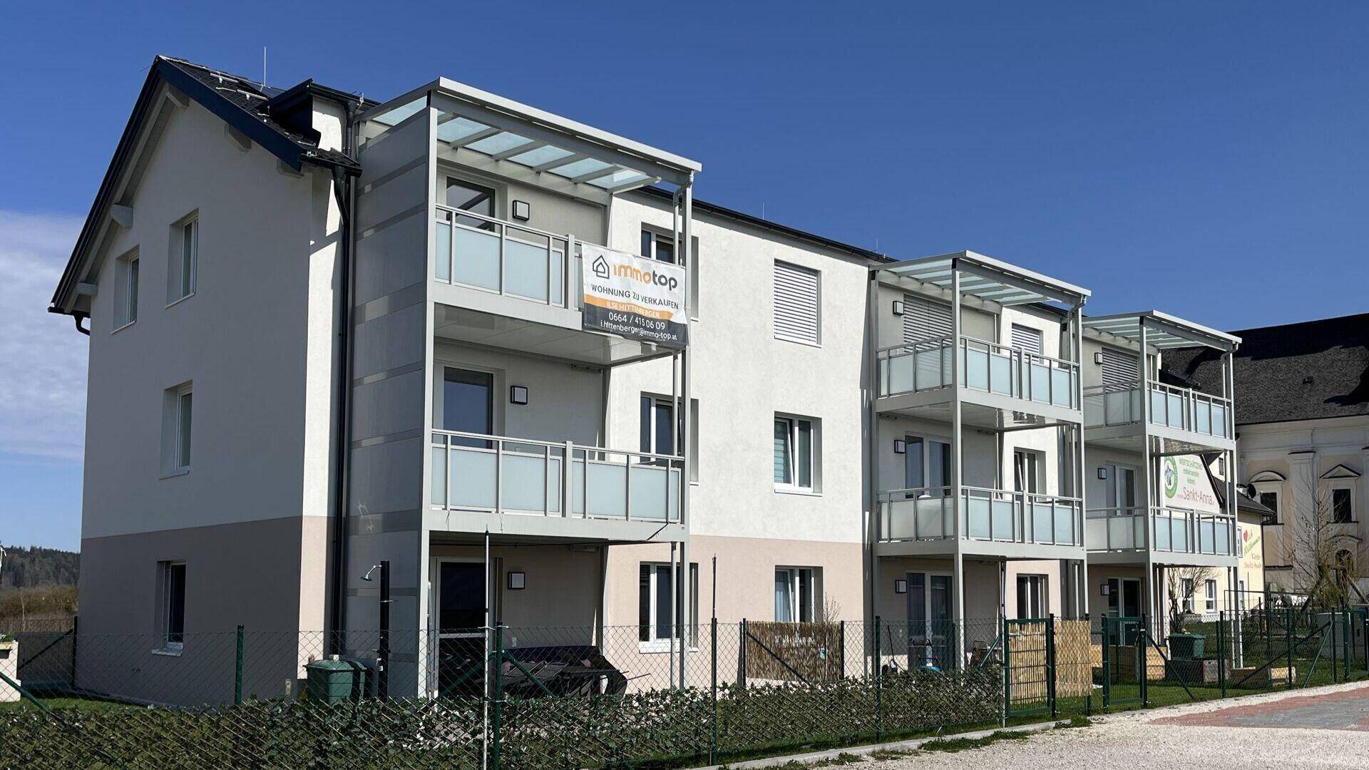 Moderne Wohnanlage mit Balkonen und Werbeschildern, umgeben von Natur.