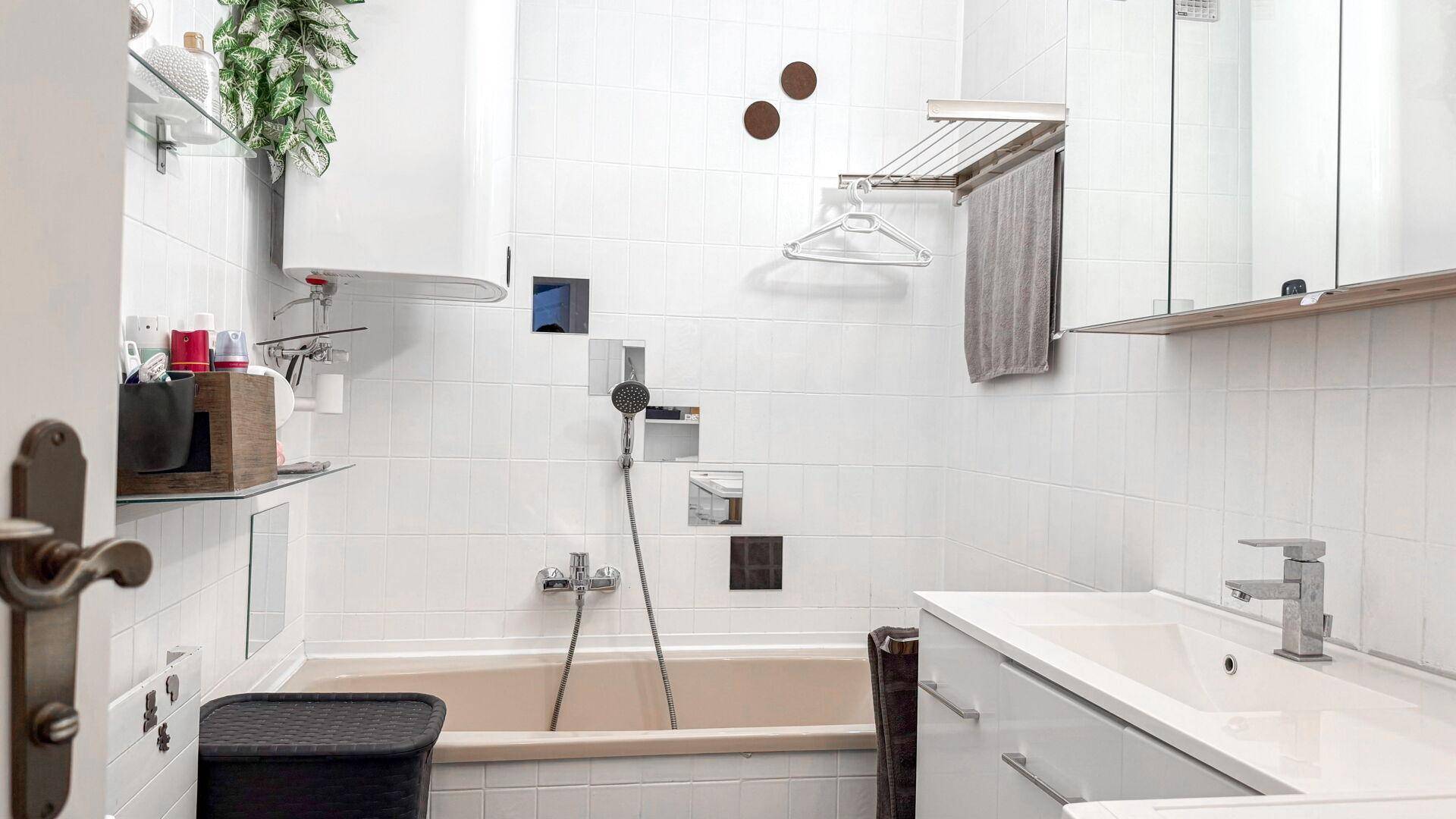 Badezimmer mit Badewanne, Waschbecken und weißen Fliesen.