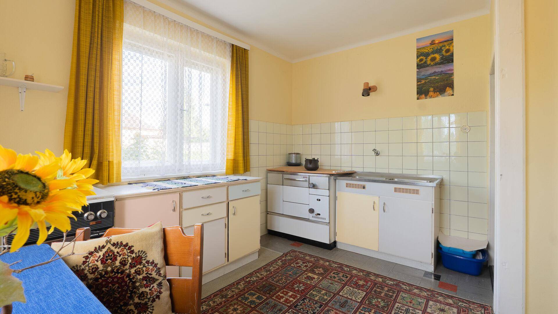 Traditionelle Küche mit gelben Fliesen, Holzofen und Essbereich am Fenster.