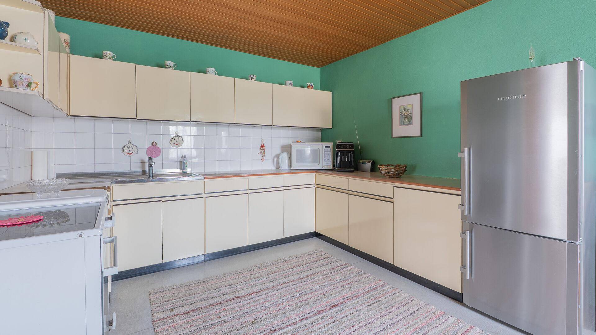 Küche mit beigen Einbauschränken, Spüle und Kühlschrank, in hellem Grün gehalten.
