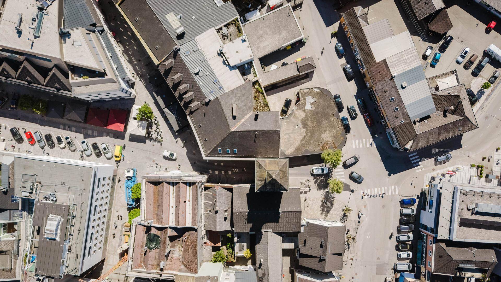 Vogelperspektive einer städtischen Bebauung mit Dächern, Straßen und parkenden Fahrzeugen.