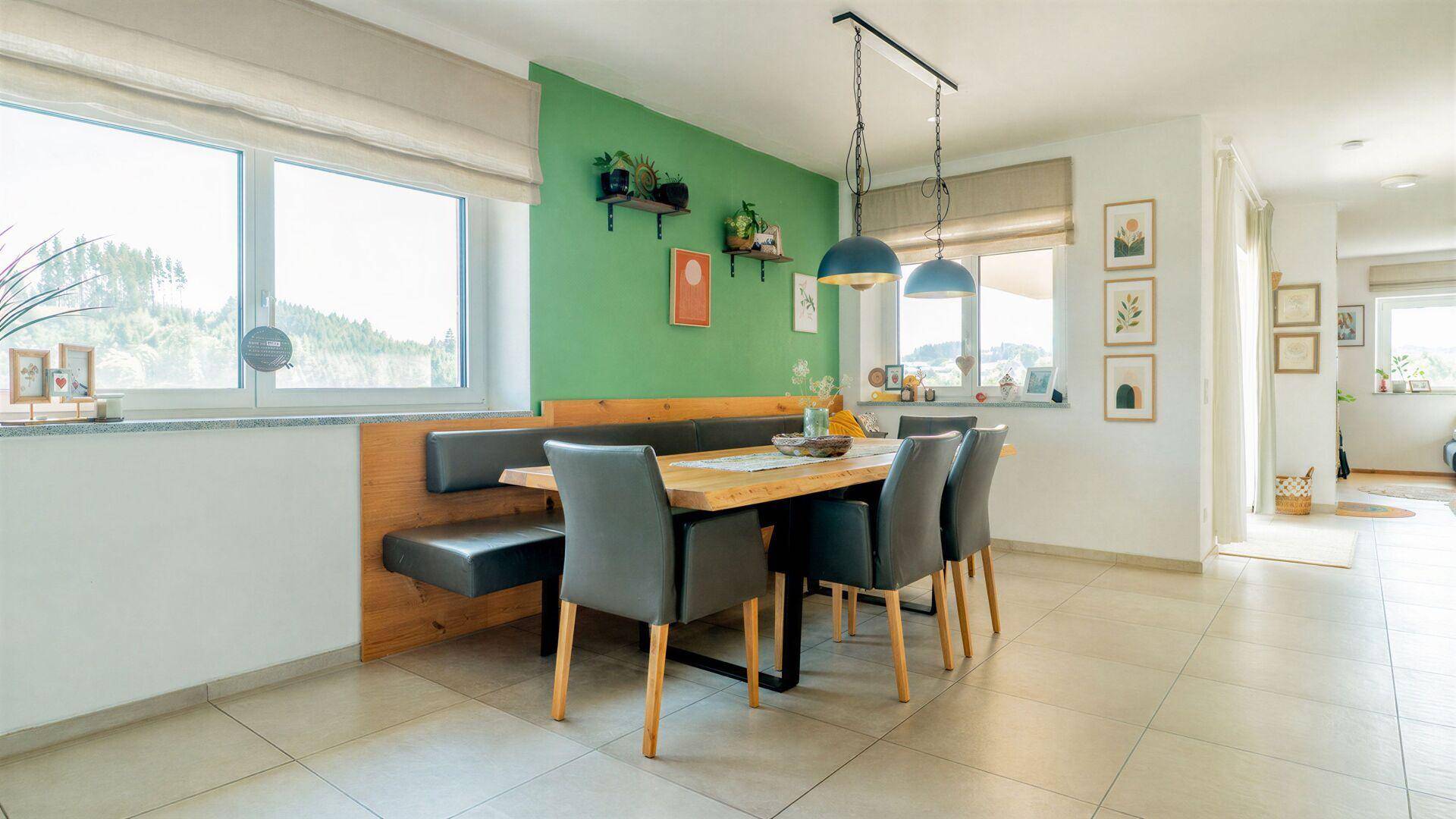 Heller Essbereich mit grüner Akzentwand, Holztisch und bequemer Sitzbank, ideal für Familien.