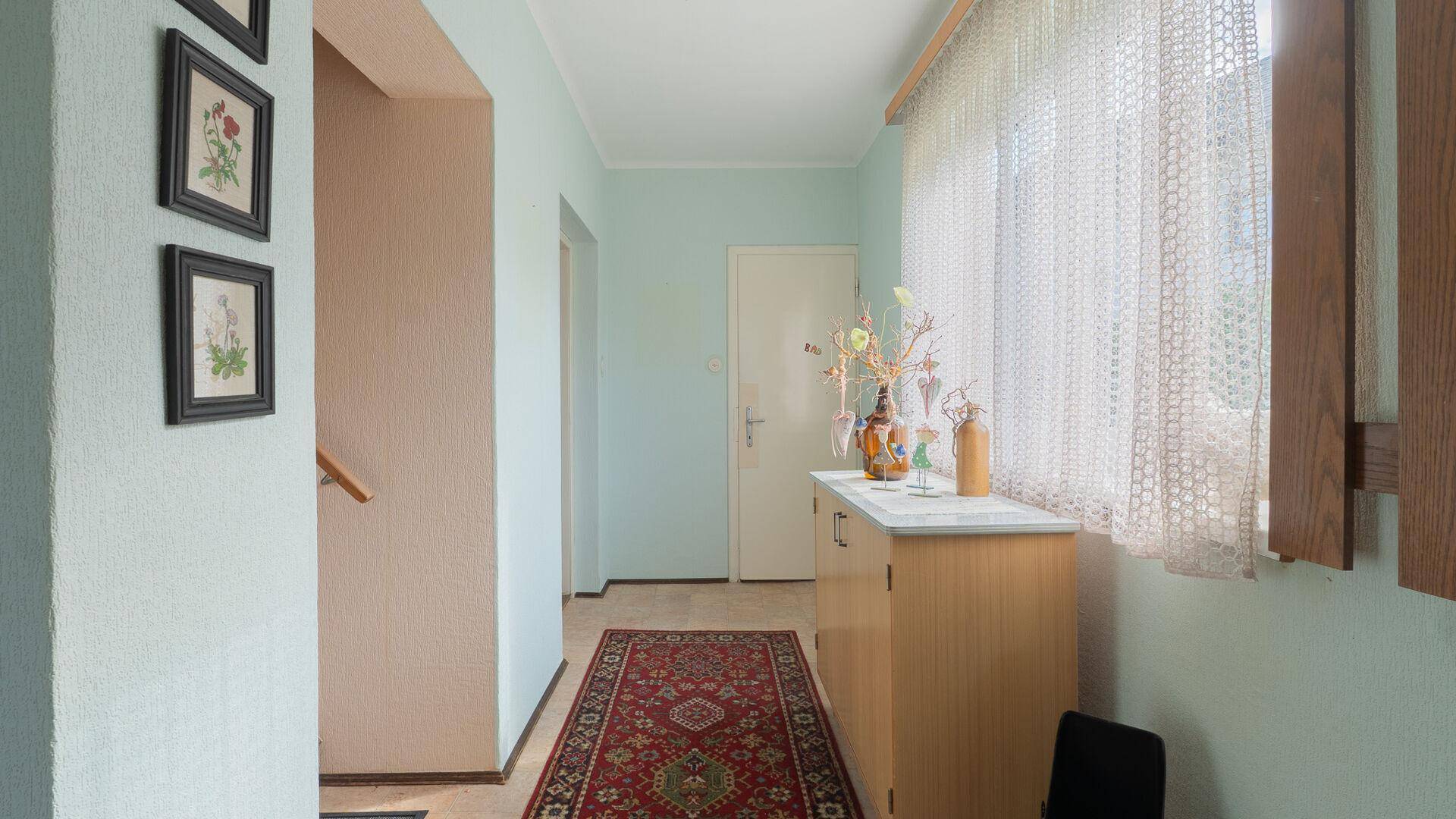 Heller Flur mit Teppichläufer, Fenster und einfacher Kommode.