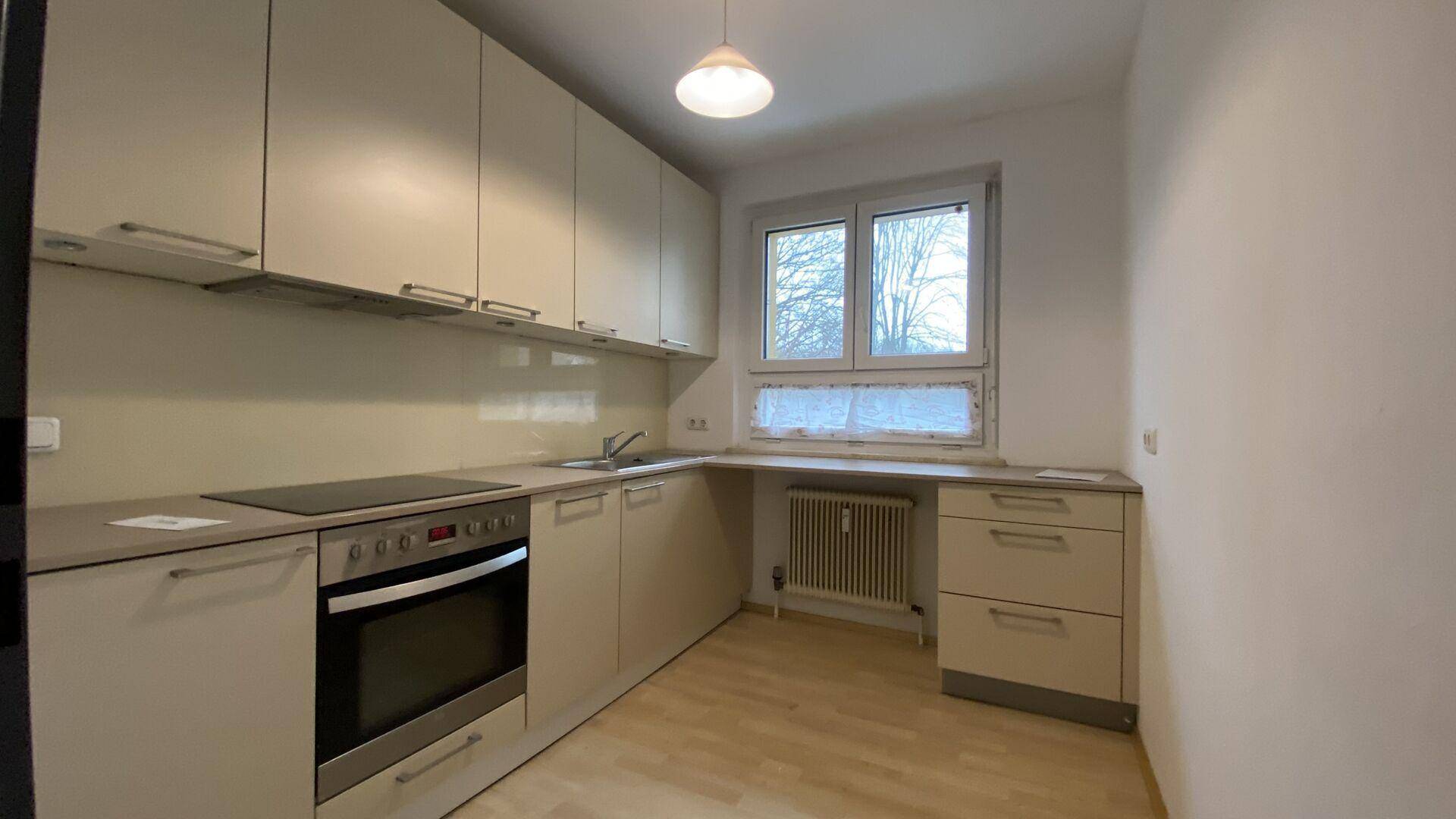 Funktionale Küche mit beigen Schränken, integrierten Geräten und Fensterblick ins Freie.