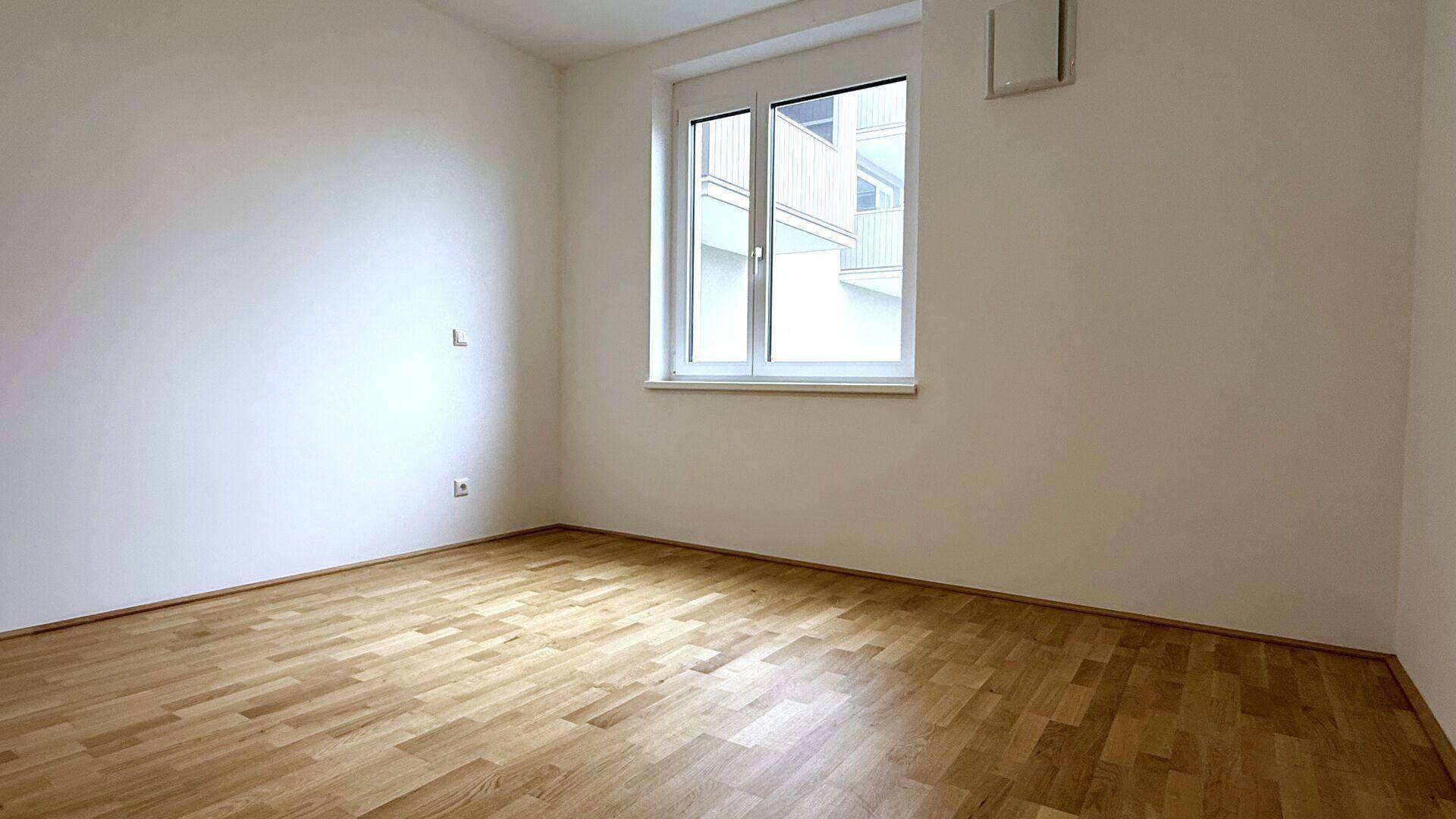 Ein weiteres helles Zimmer mit Holzboden und einem Fenster, das einen Blick nach draußen ermöglicht.