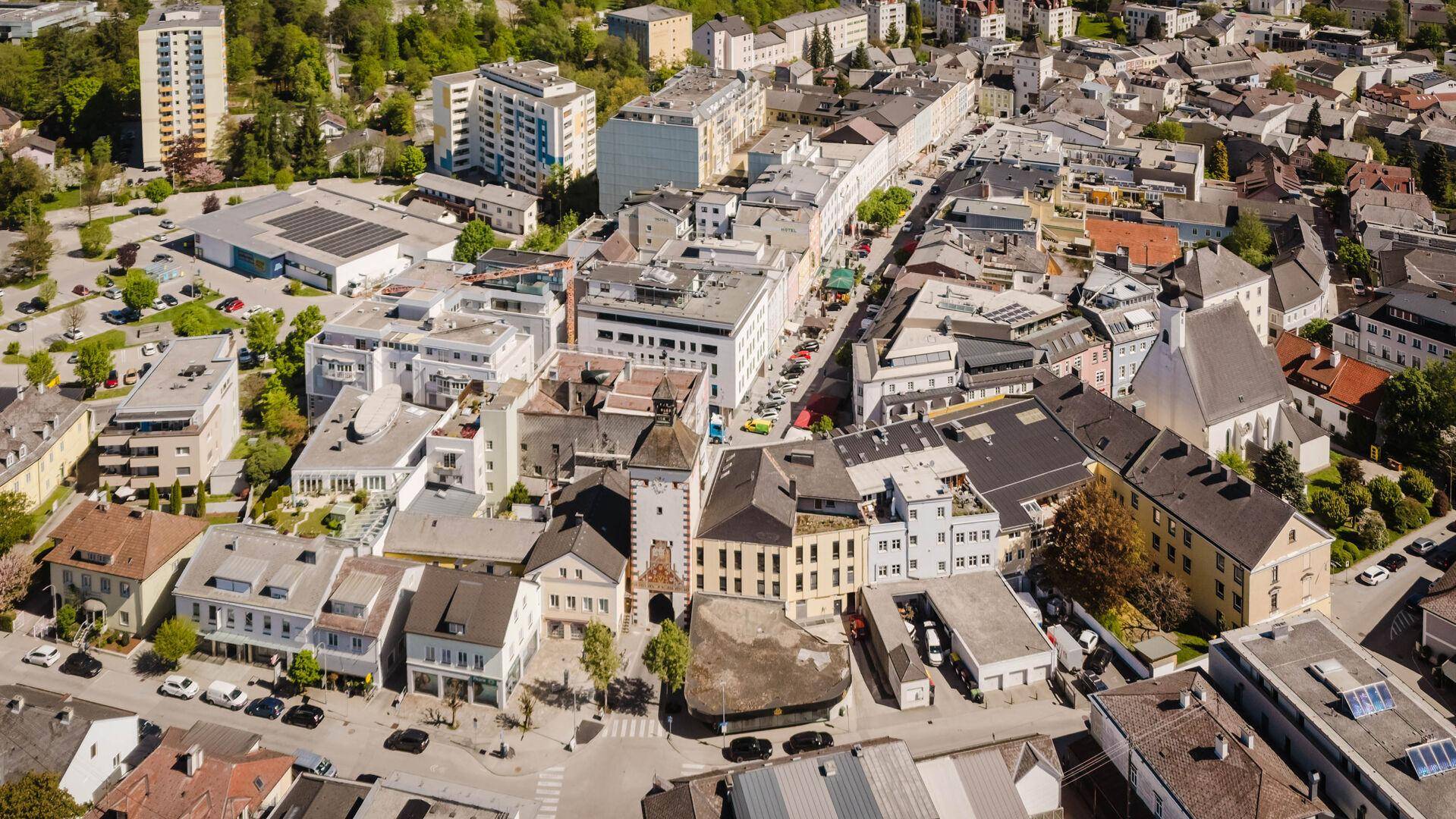 Weitläufige Luftaufnahme einer Stadt mit vielen Gebäuden, Straßen und Grünflächen unter blauem Himmel.