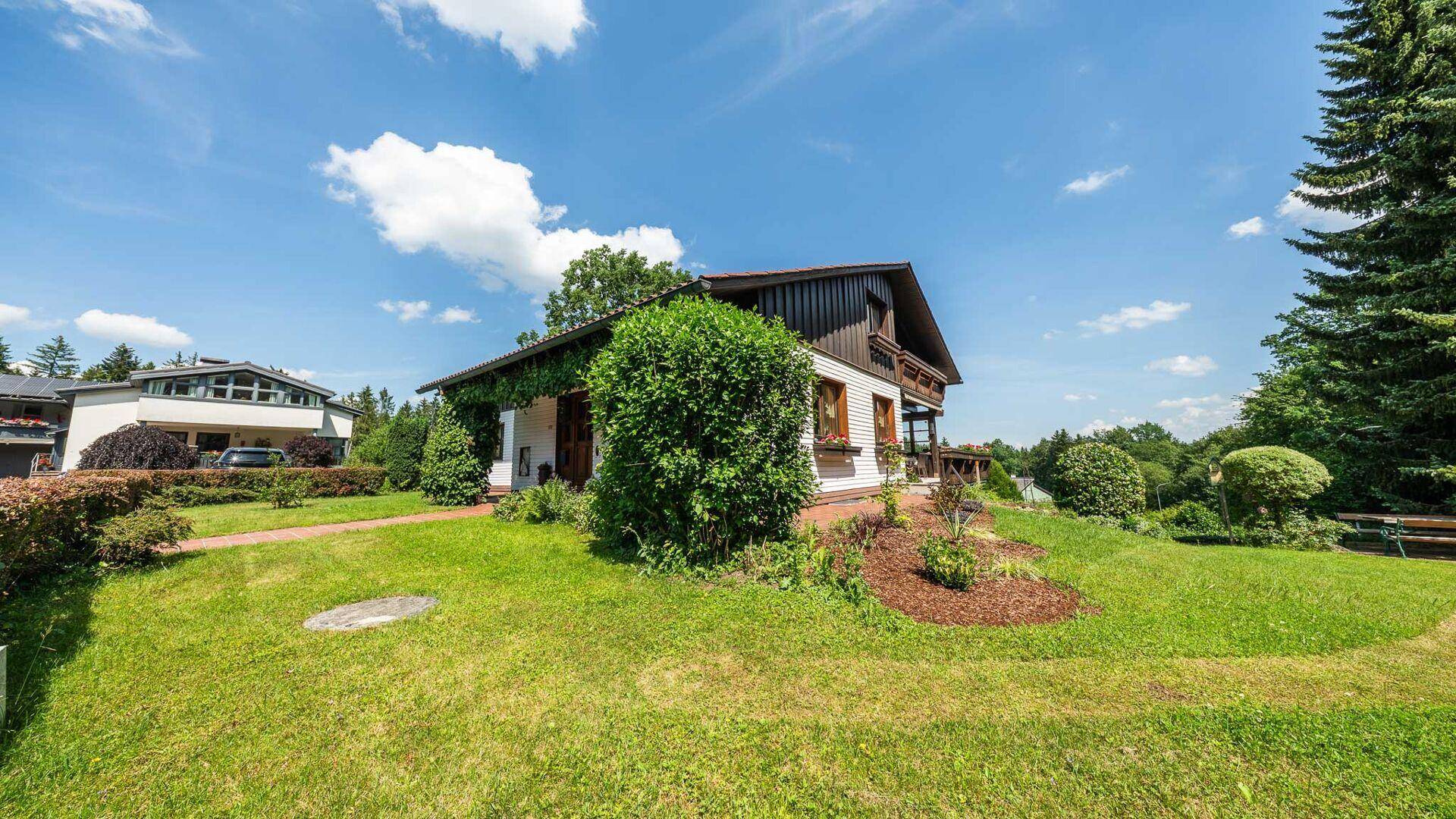 Seitliche Ansicht des Hauses mit überdachtem Eingang und gepflegtem Garten, umgeben von viel Grün.