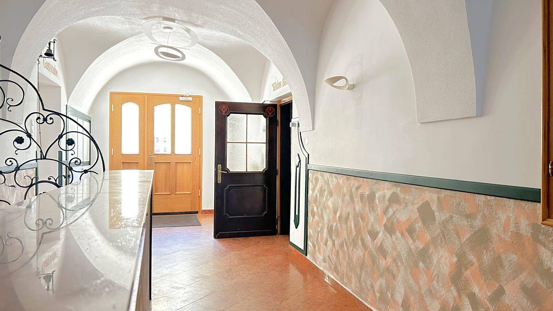 Gewölbter Flur mit Terrakotta-Bodenfliesen, dekorativer Wandgestaltung und Holztüren.