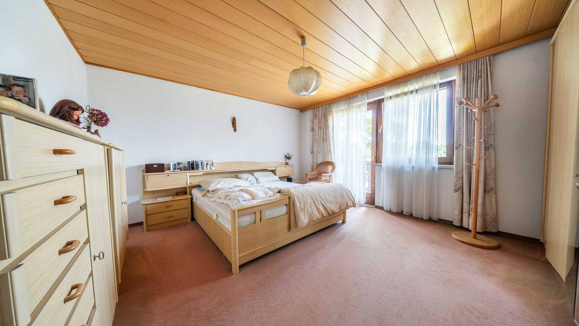 Helles Schlafzimmer mit Holzdecke, Teppichboden und Zugang zu einem Balkon.
