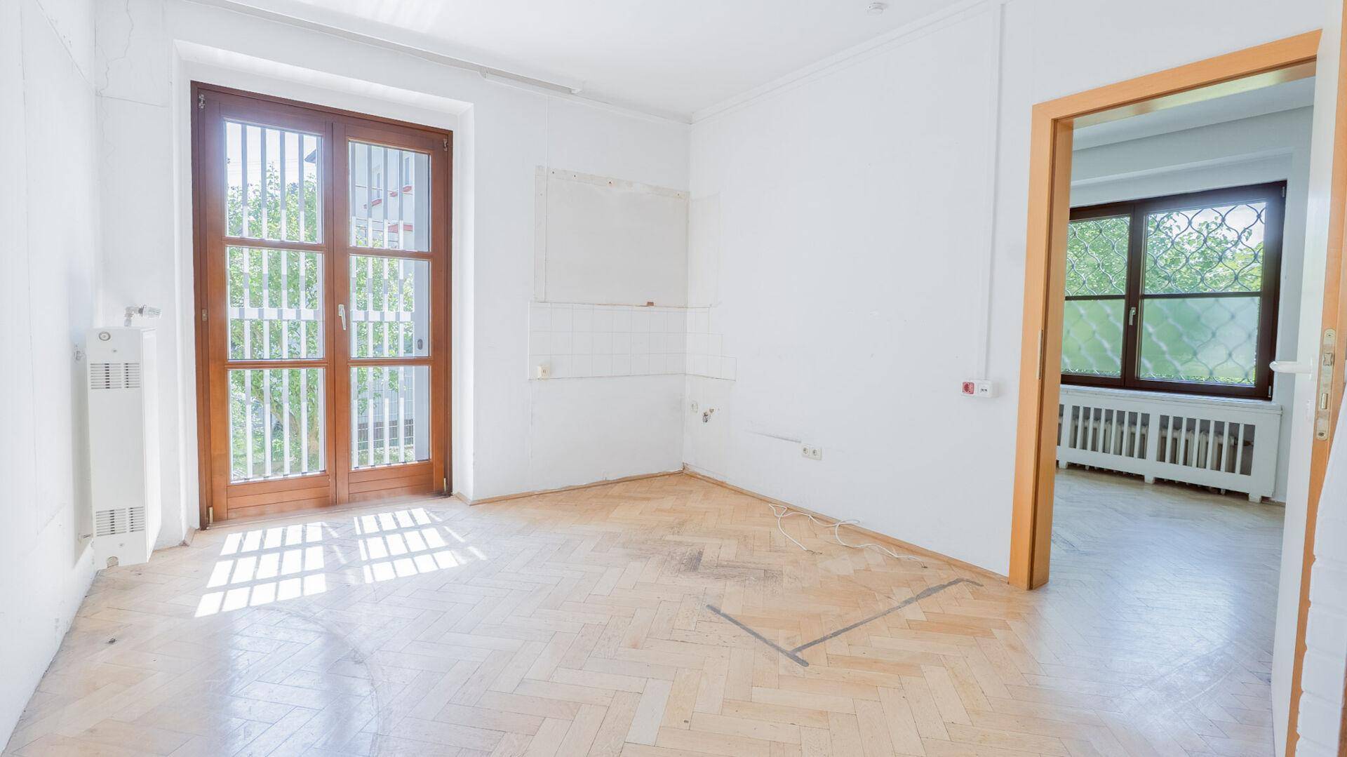 Leerer Raum mit Fischgrätparkett und Fenstertür, die viel Licht hereinlässt.