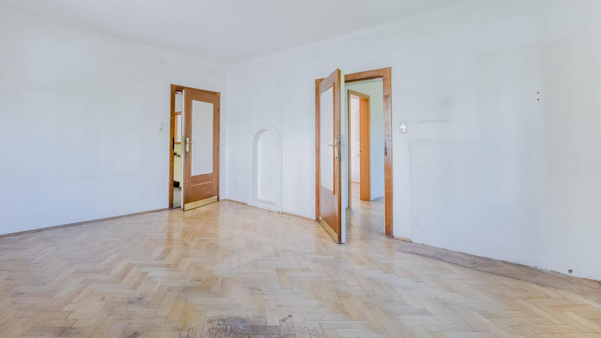 Geräumiger leerer Raum mit Fischgrätparkett und mehreren Holztüren, bereit zur Gestaltung.