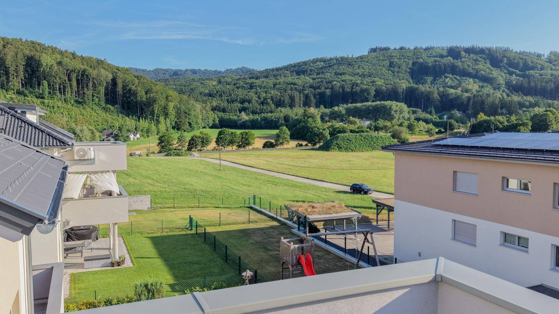 Blick auf eine Wohnsiedlung mit Spielplatz, umgeben von grünen Feldern und Wäldern.