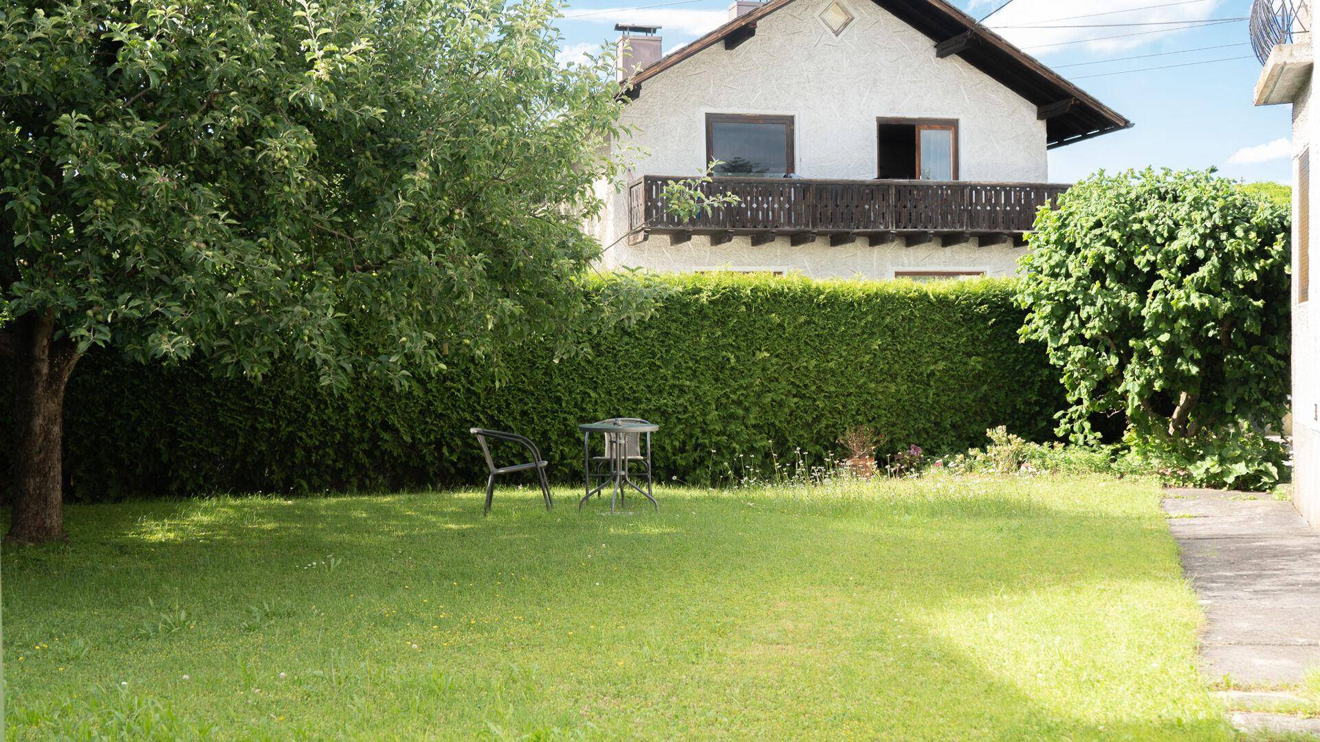Grüner Gartenbereich mit Rasenfläche, Bäumen und einer kleinen Sitzgelegenheit.