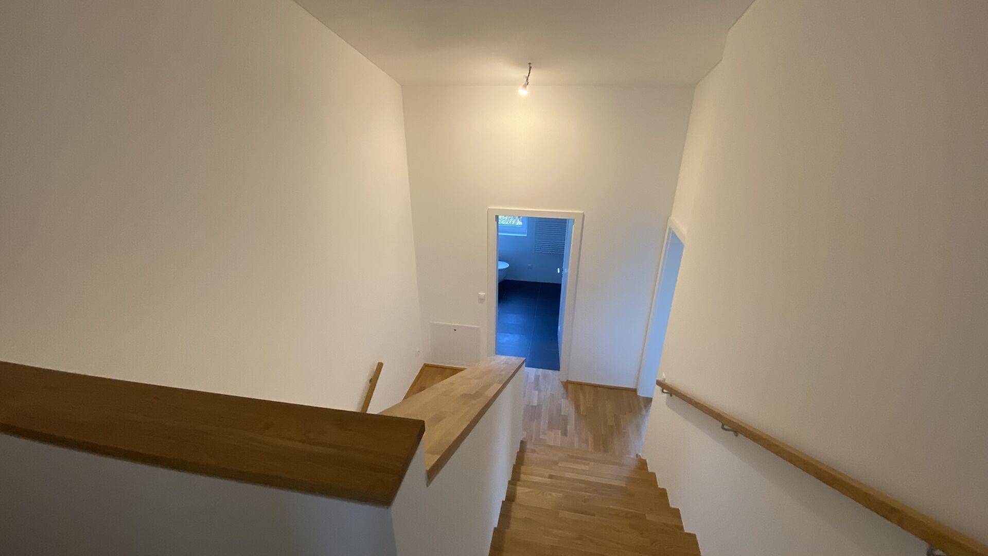 Helles Treppenhaus mit Holzstufen und Geländer, verbindet die Wohnebenen.