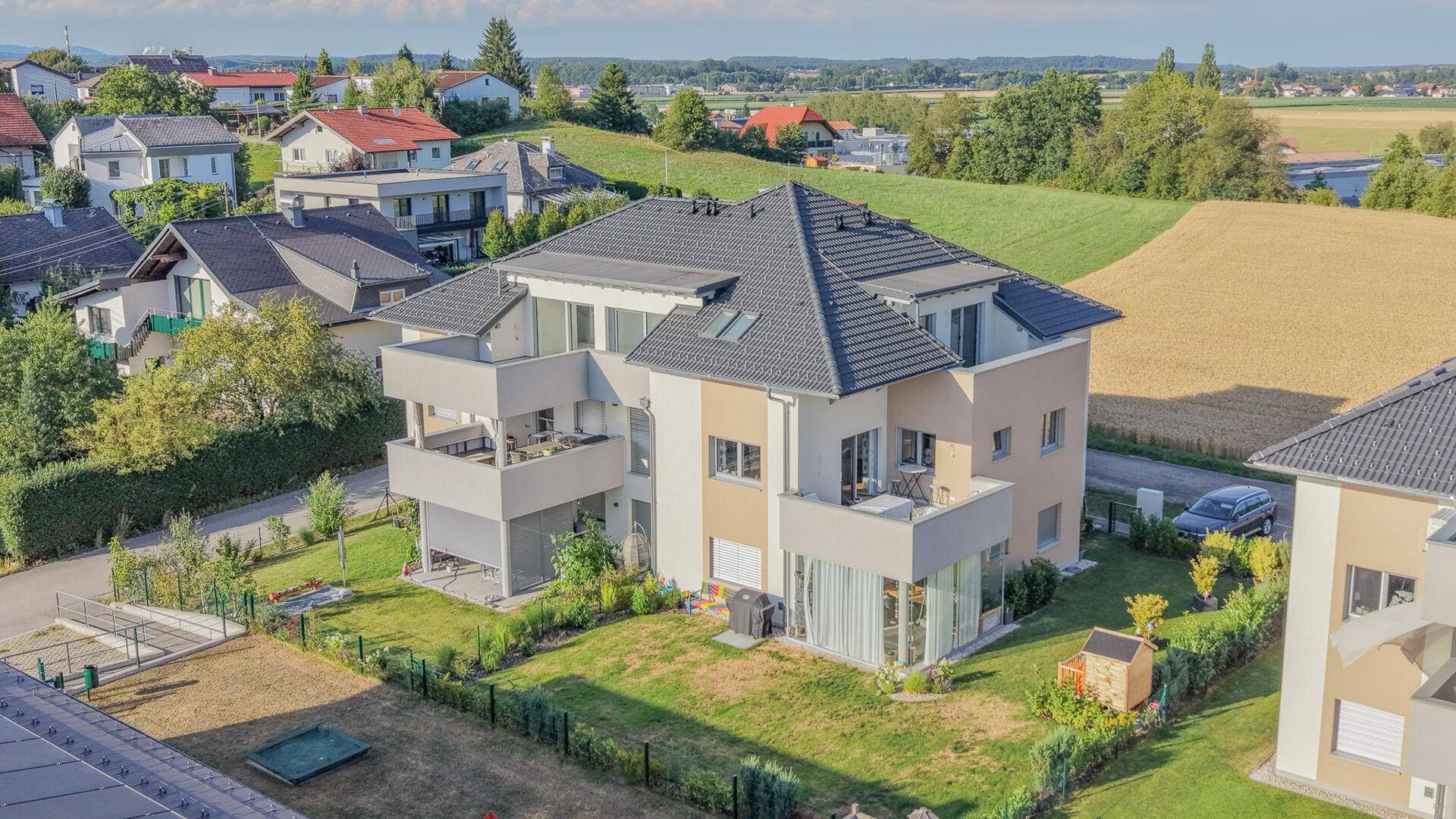 Luftaufnahme eines modernen Wohngebäudes mit Balkonen, Garten und angrenzenden Feldern.
