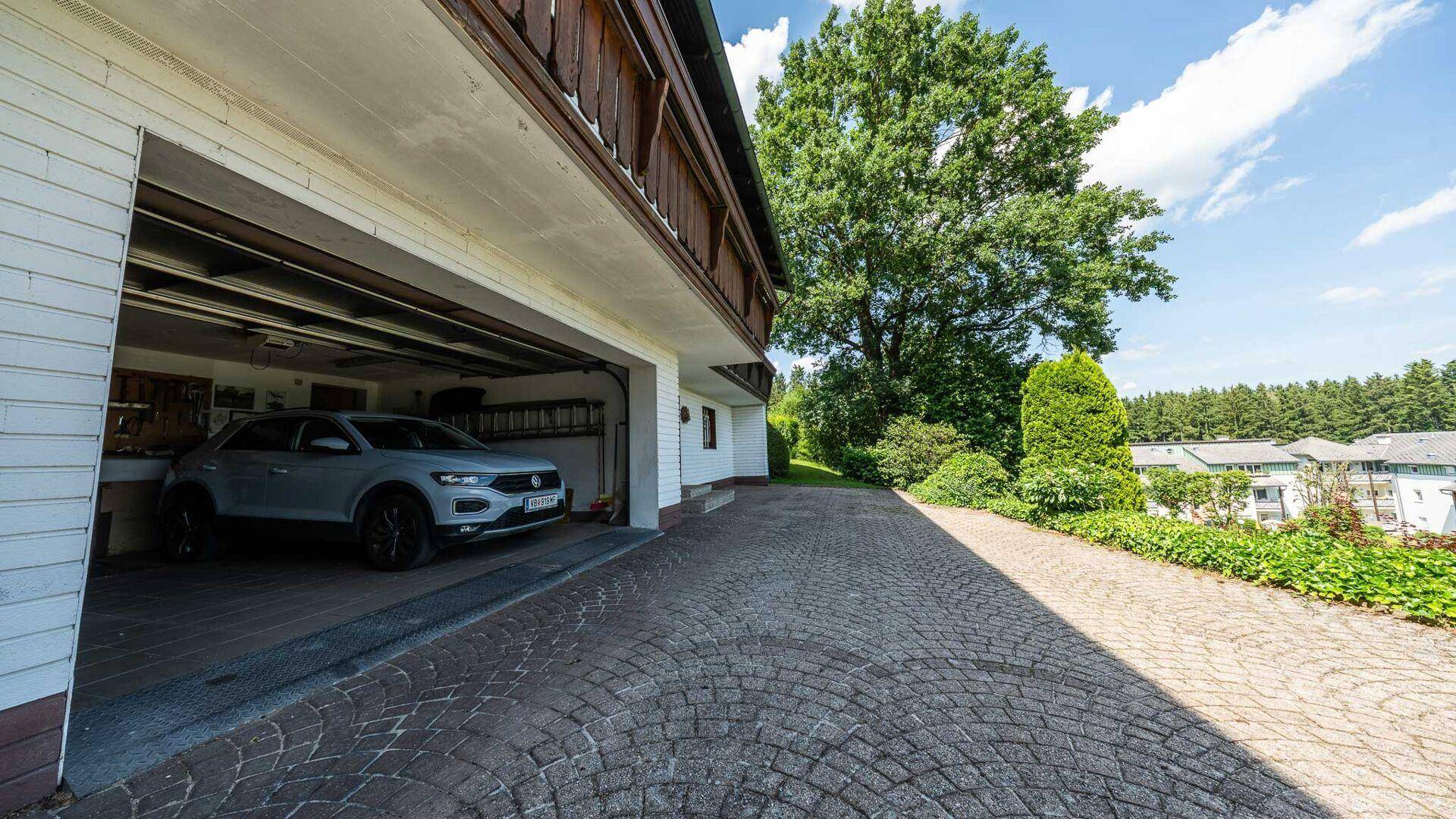 Offene Garage mit einem geparkten Auto und gepflasterter Auffahrt zum Haus.
