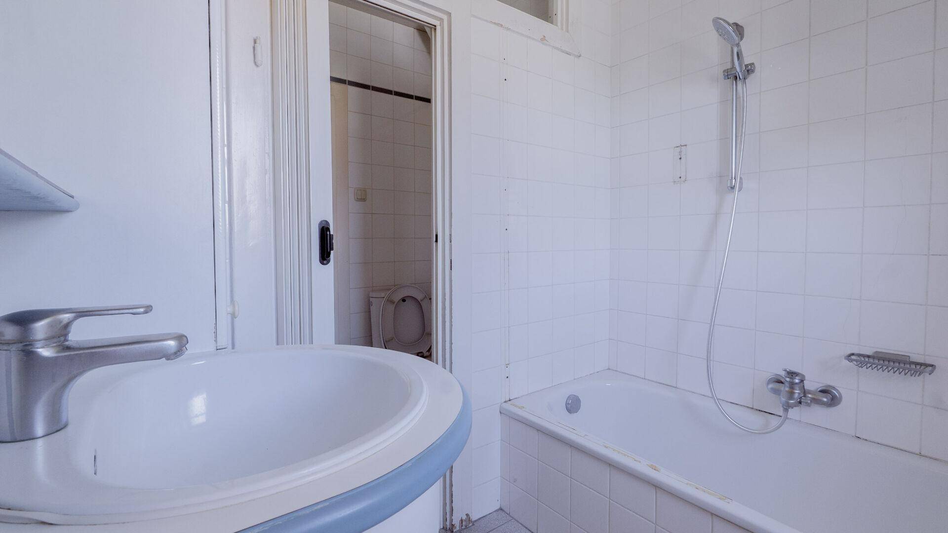 Einfaches Badezimmer mit Badewanne, Waschbecken und weißen Fliesen, renovierungsbedürftig.