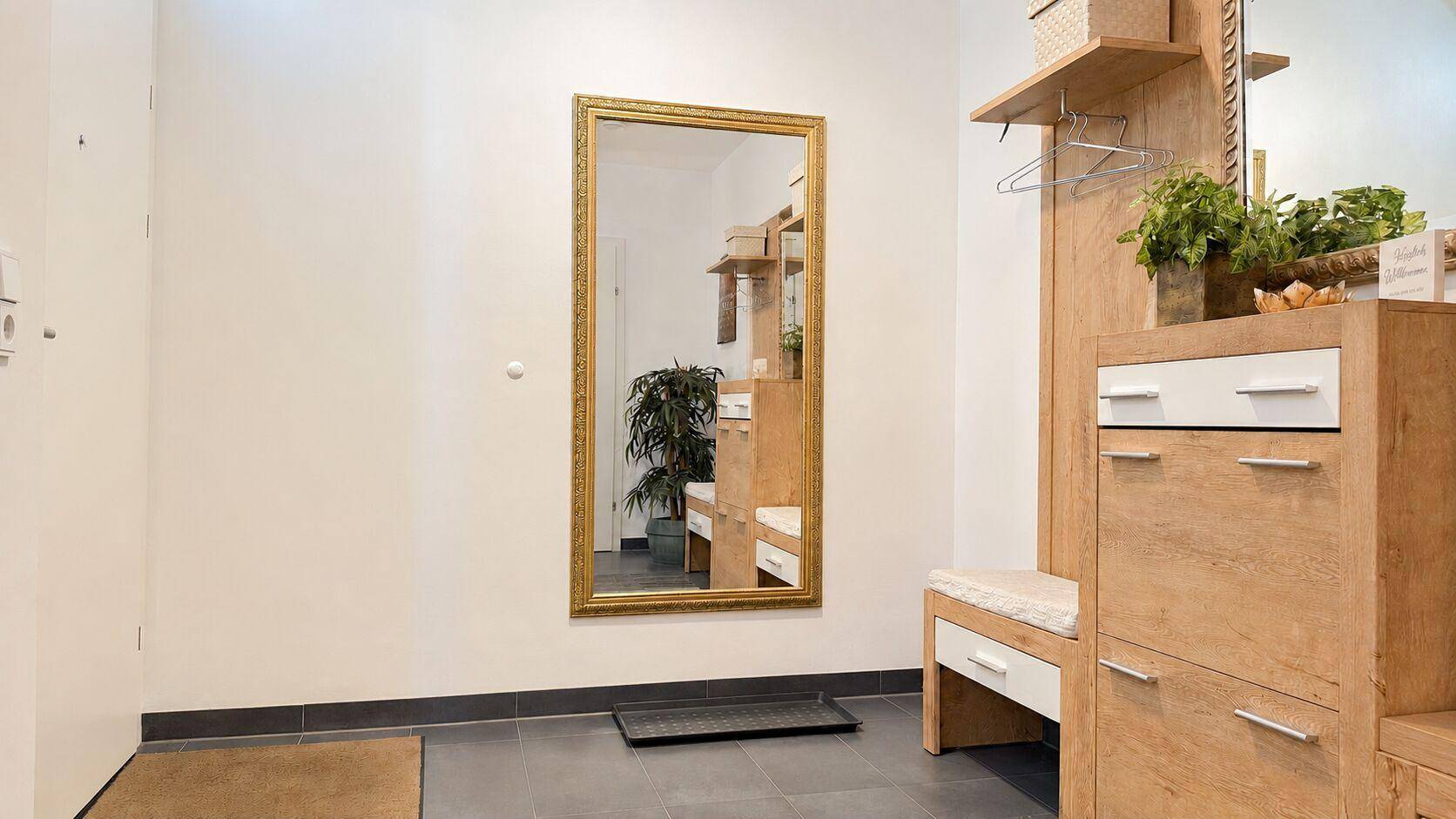 Heller Eingangsbereich mit großem Spiegel und praktischen Holzmöbeln für Garderobe und Stauraum.