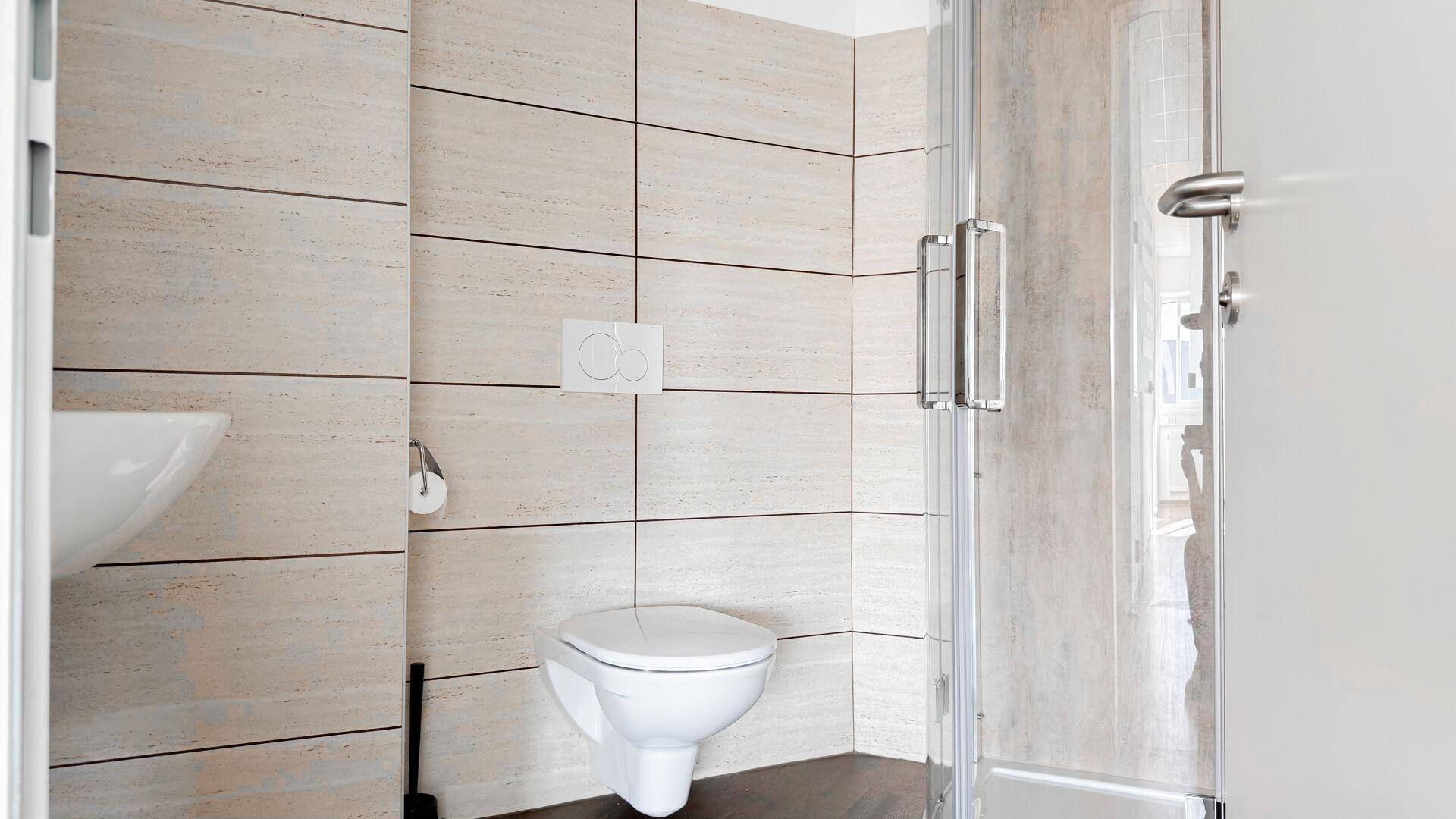 Modernes Badezimmer mit beigefarbenen Fliesen, wandhängendem WC und Duschkabine, sehr gepflegt.