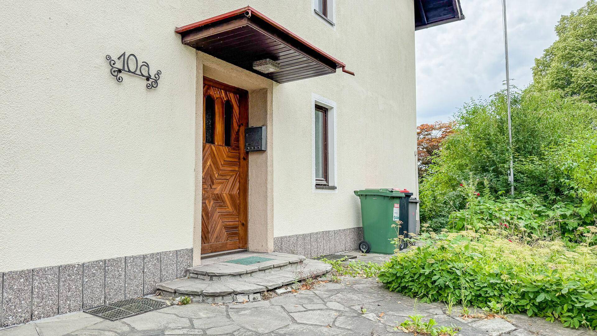 Eingangsbereich des Hauses mit Holztür, Vordach und gepflastertem Zugangsweg.