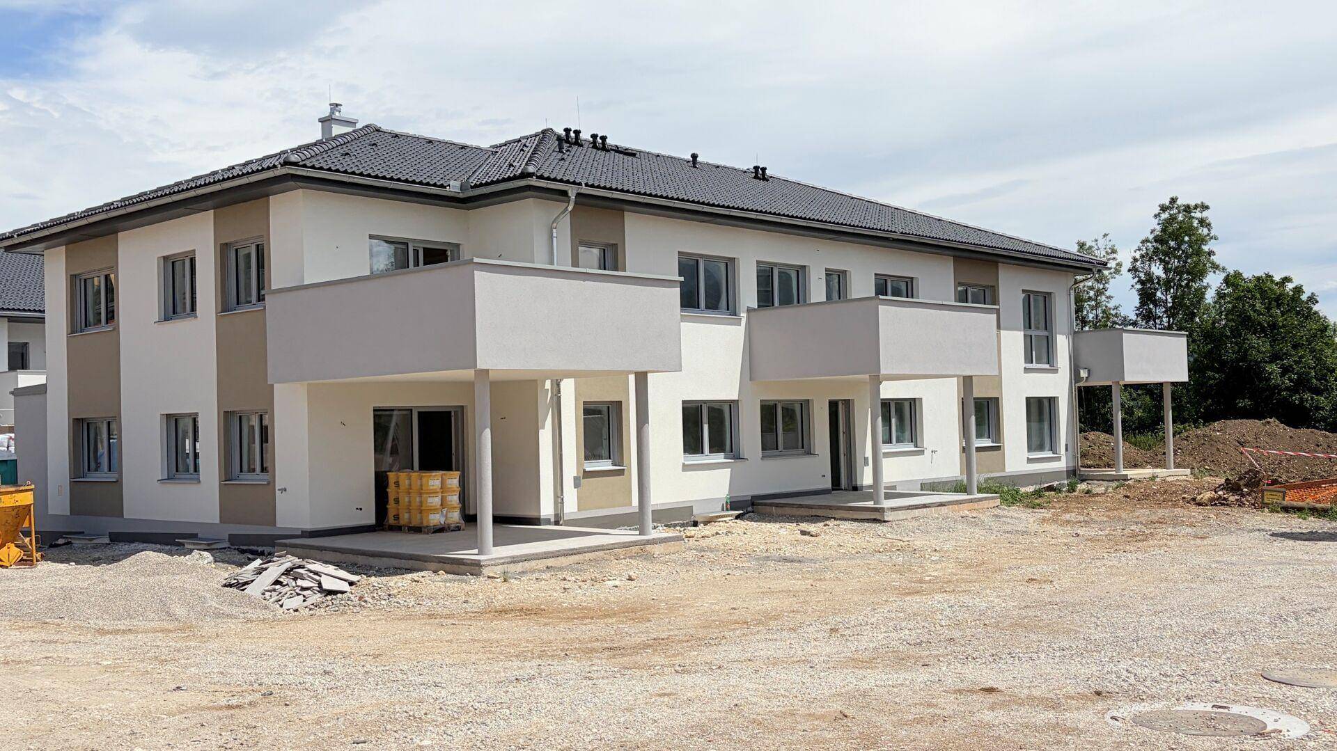 Neubaugebäude mit moderner Architektur, weißer Fassade und angrenzender Baustelle im Vordergrund.