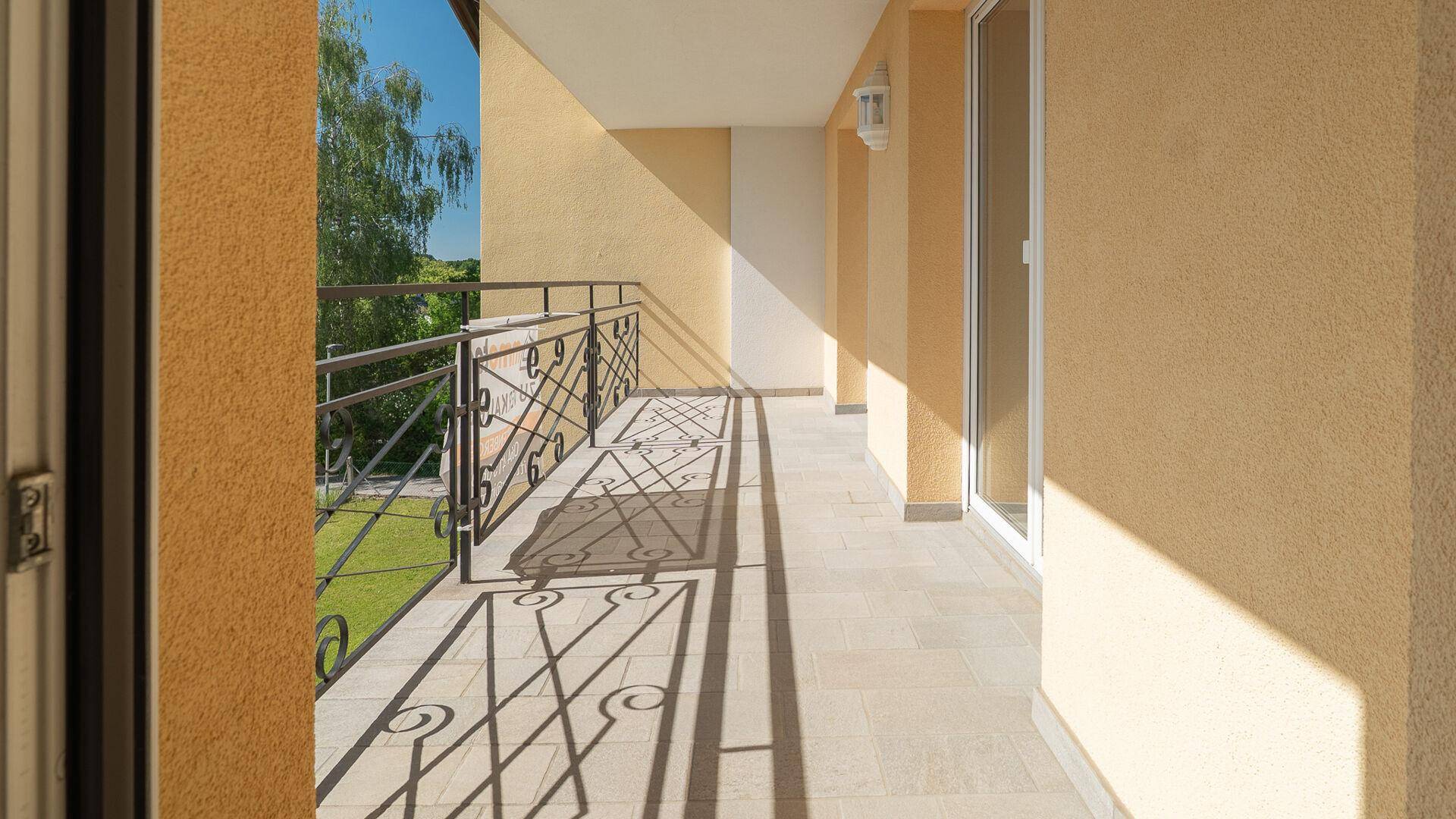 Langer Balkon mit schmiedeeisernem Geländer und Fliesenboden, ideal für sonnige Stunden.