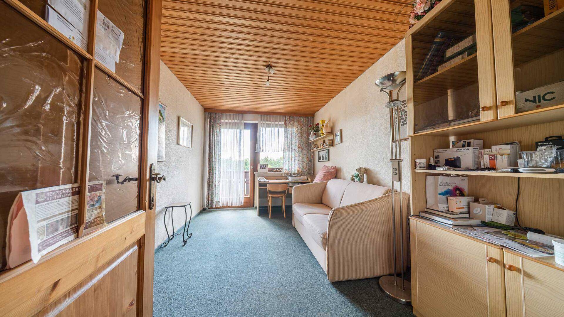 Helles Zimmer mit Teppichboden, Holzdecke und Zugang zu einem Balkon.