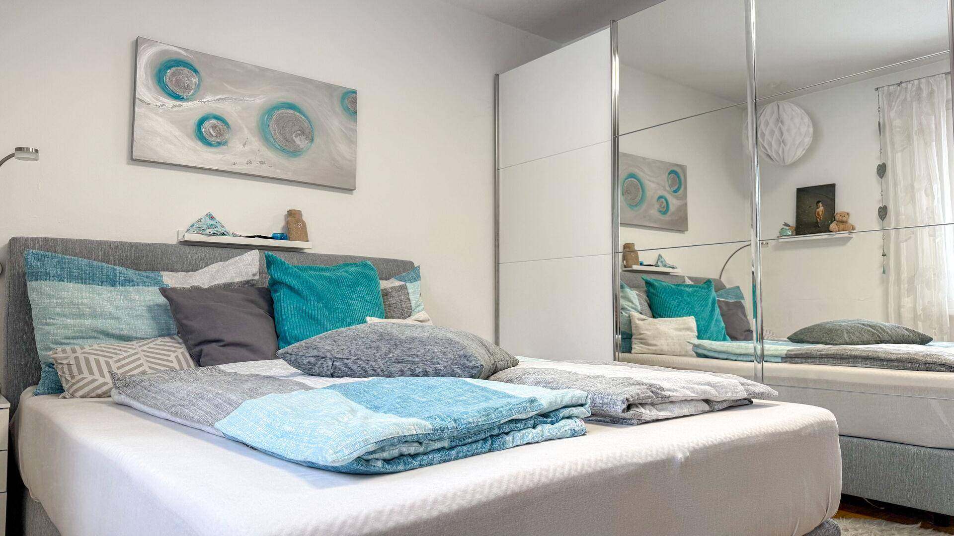 Helles Schlafzimmer mit Doppelbett, Spiegelschrank und moderner Wanddekoration.