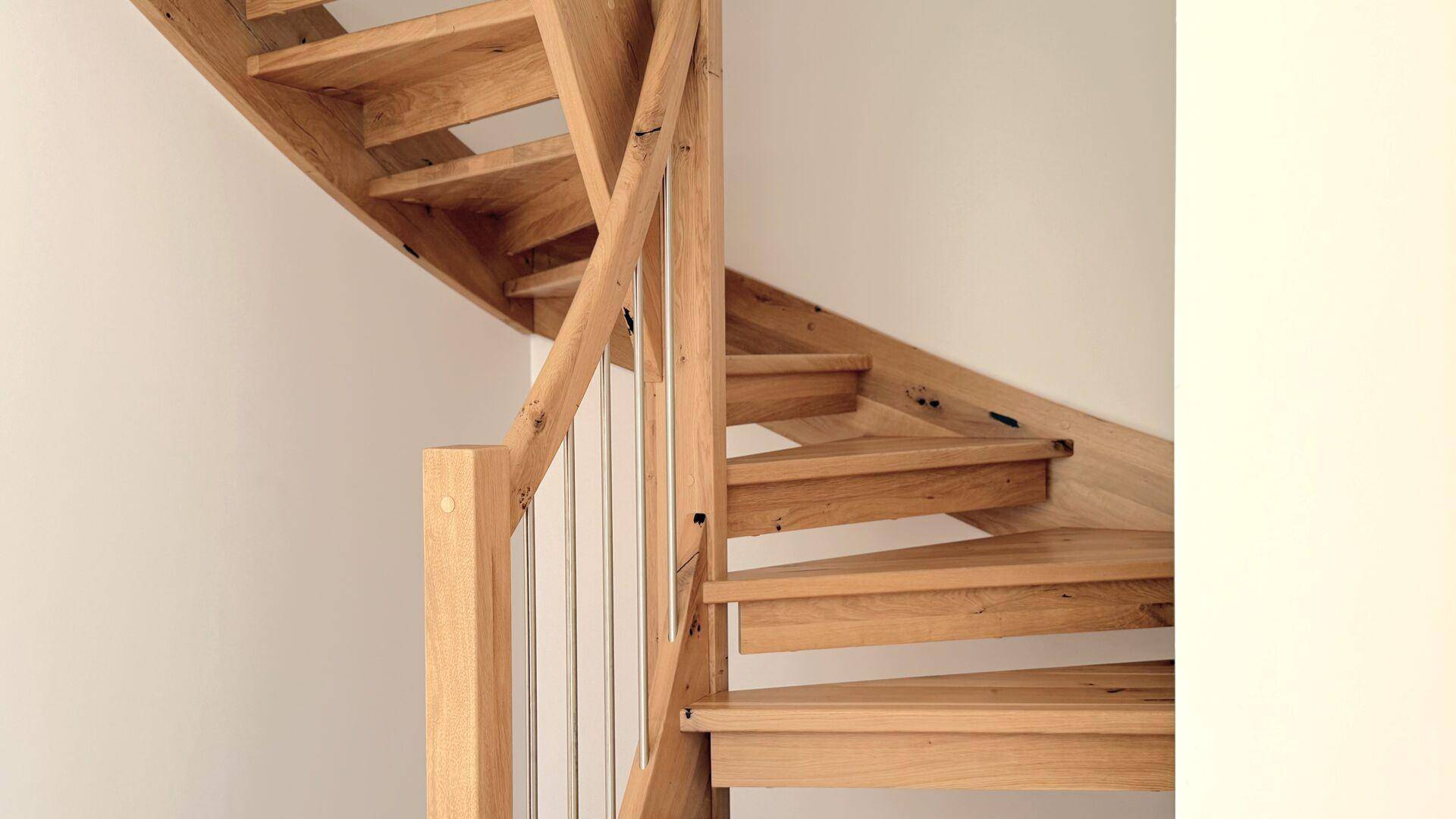 Detailansicht einer modernen Holztreppe mit filigranem Geländer, die die Stockwerke verbindet.
