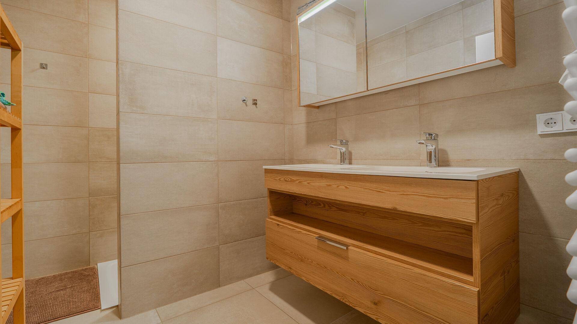 Modernes Badezimmer mit Doppelwaschbecken, Holzunterschrank und großem Spiegelschrank.