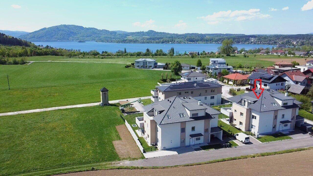 Luftaufnahme einer Wohnanlage mit Seeblick, umgeben von Feldern und weiteren Häusern.