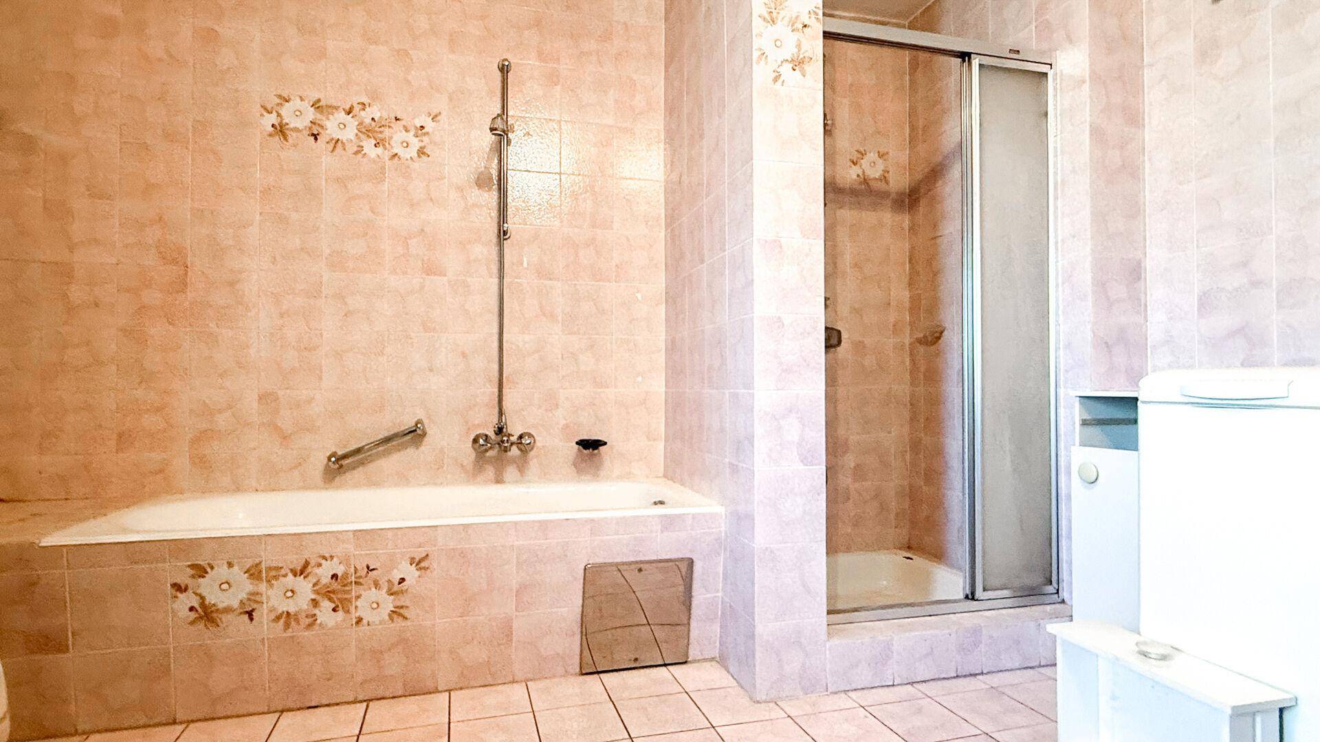 Badezimmer mit Badewanne und Duschkabine, gefliest in rosa Tönen mit floralen Akzenten.