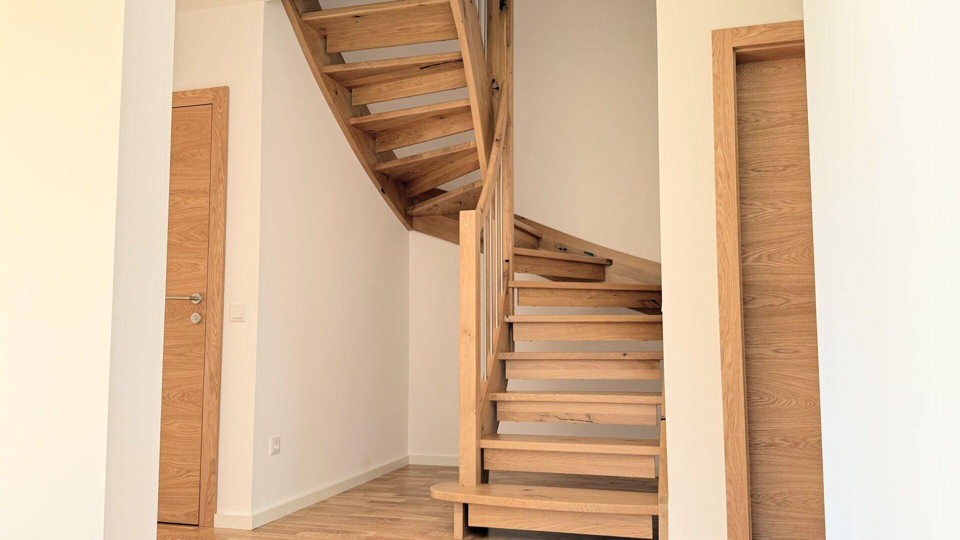 Heller Flur mit einer modernen Holztreppe und Holztüren, die zu den oberen Etagen führen.